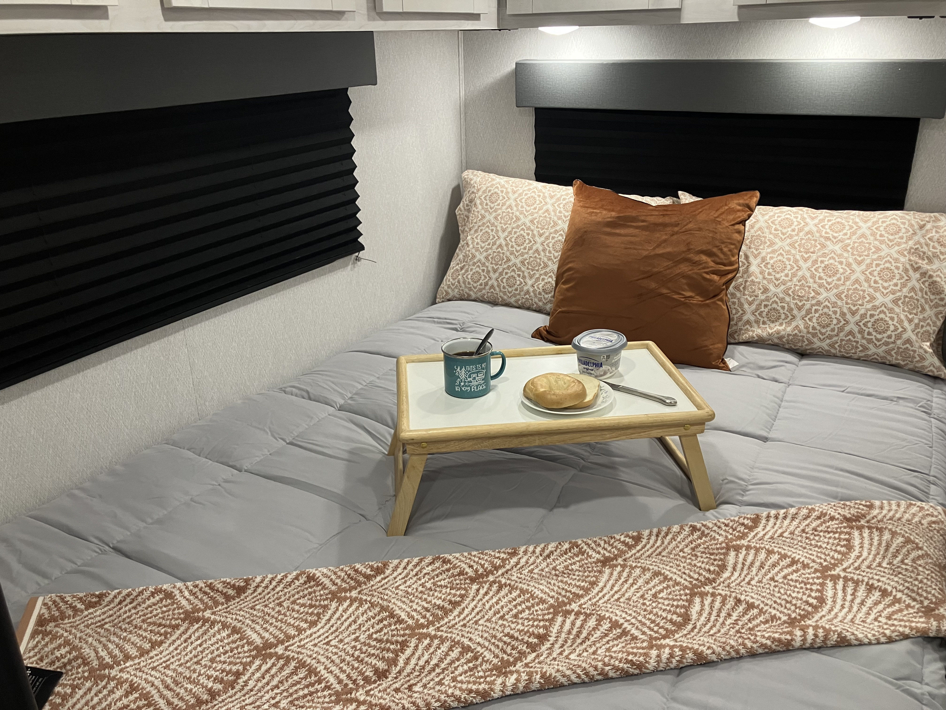 Cozy RV rental bedroom setup with breakfast in bed: coffee, bagel, cream cheese on a tray, with comfy pillows & decor.. Forest River East to West Entrada 210NS 2025