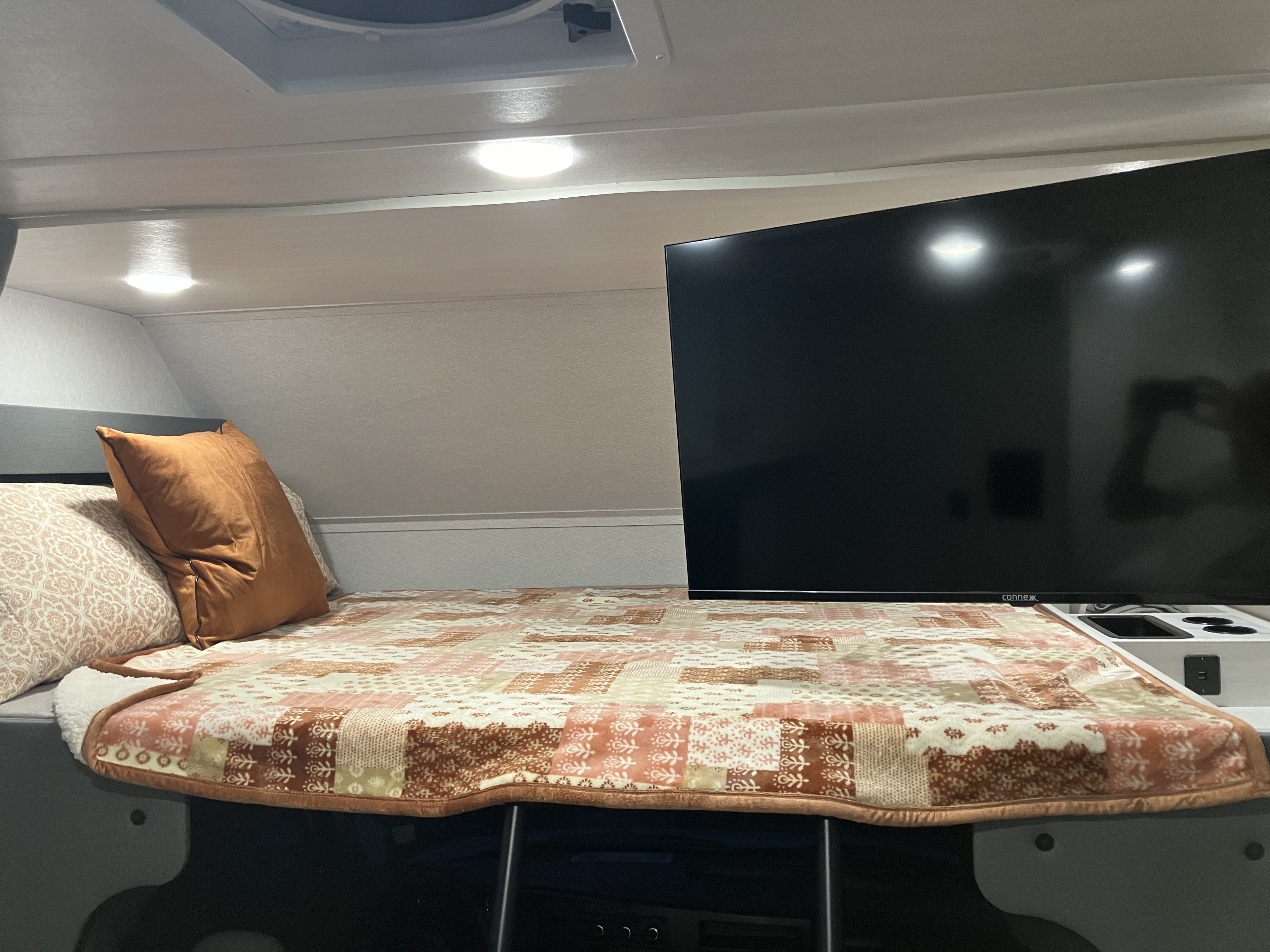 This cozy RV rental features a compact bedroom with a soft quilt, comfortable pillows, and a large TV.. Forest River East to West Entrada 210NS 2025