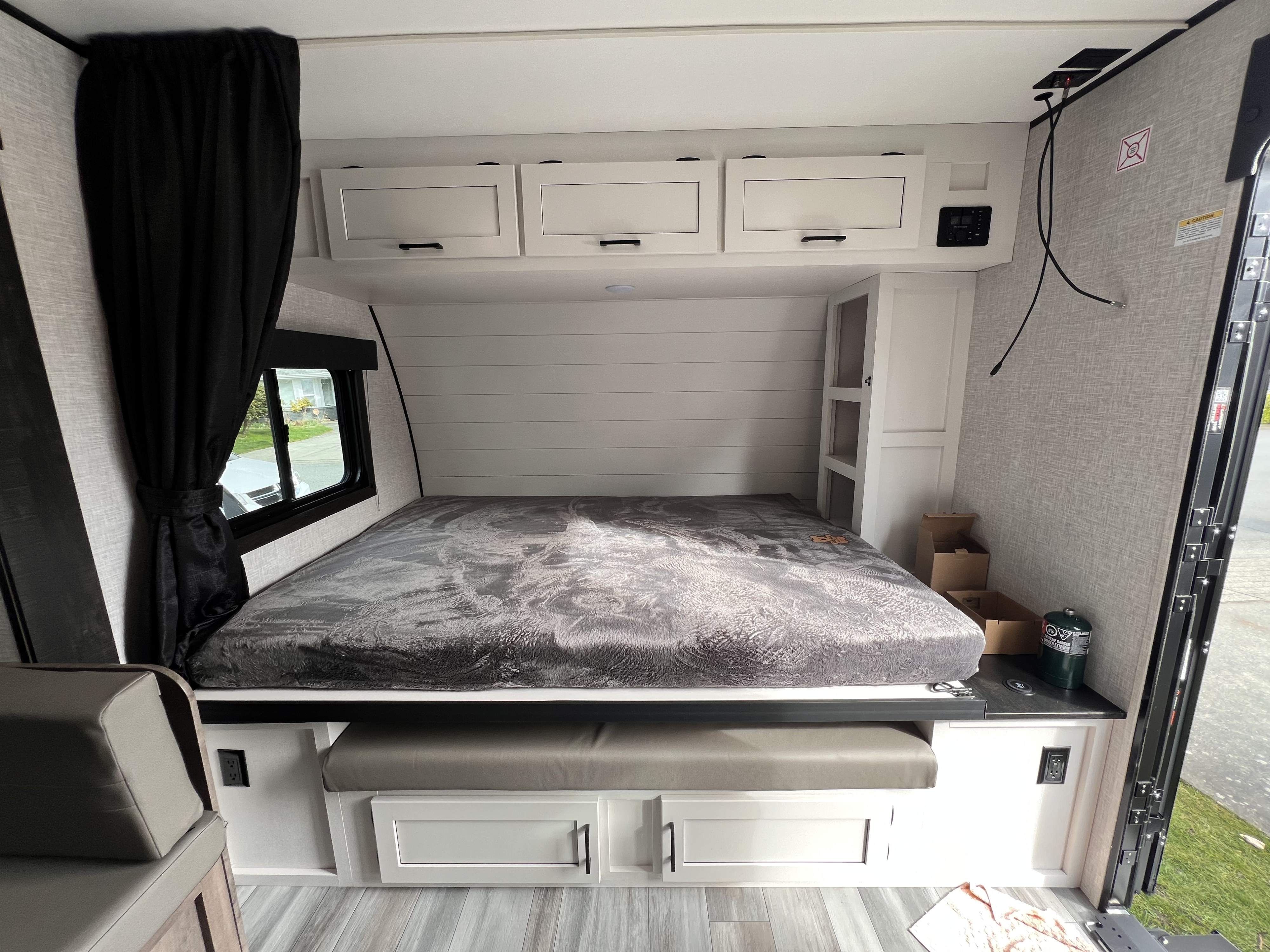 Bright RV rental sleeping area with gray bed, white overhead cabinets, bench seat, and window.. Highland Ridge RV Open Range 2024