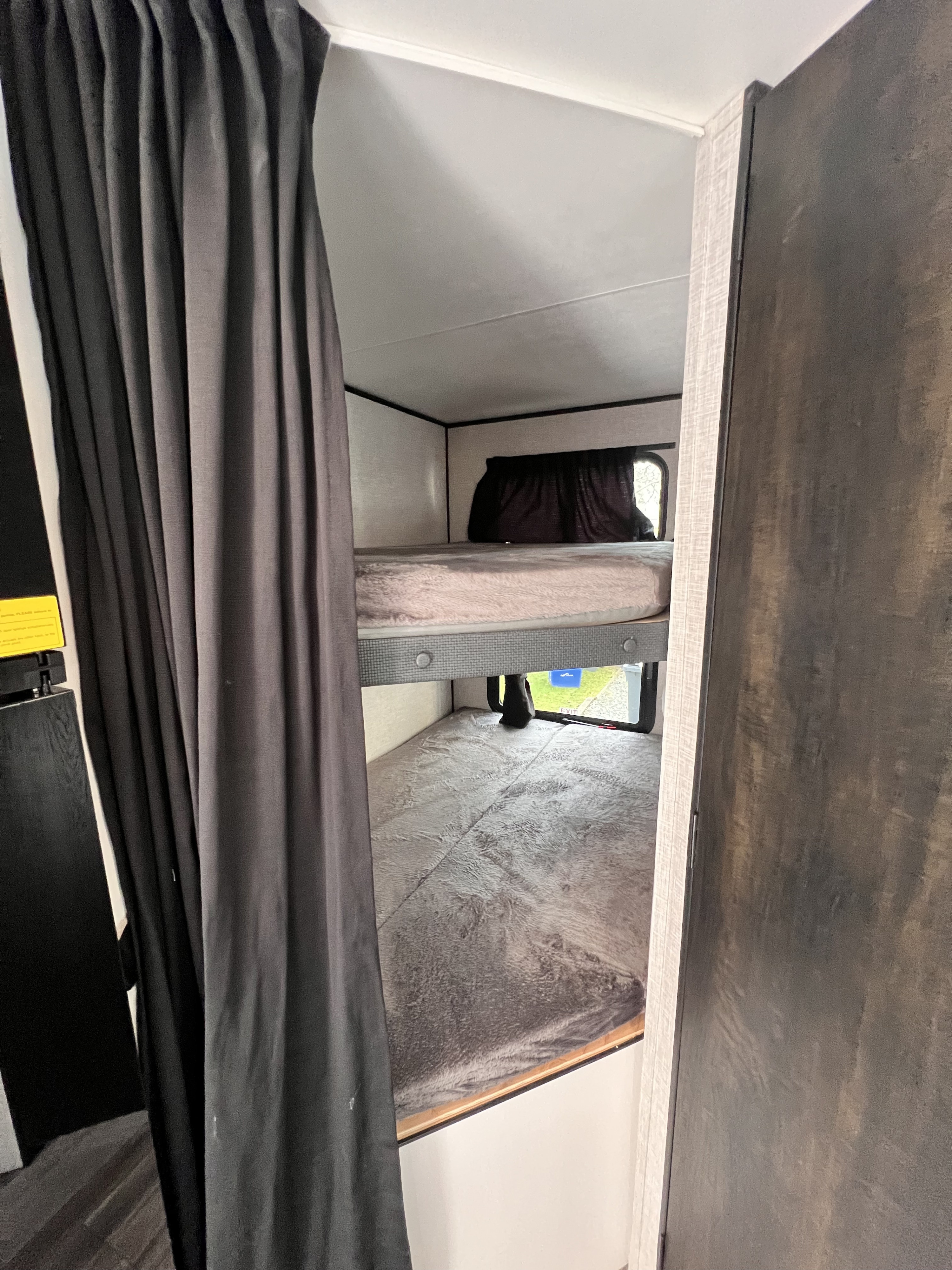 View inside an RV rental showing two neatly made bunk beds with soft gray bedding and a dark privacy curtain.. Highland Ridge RV Open Range 2024