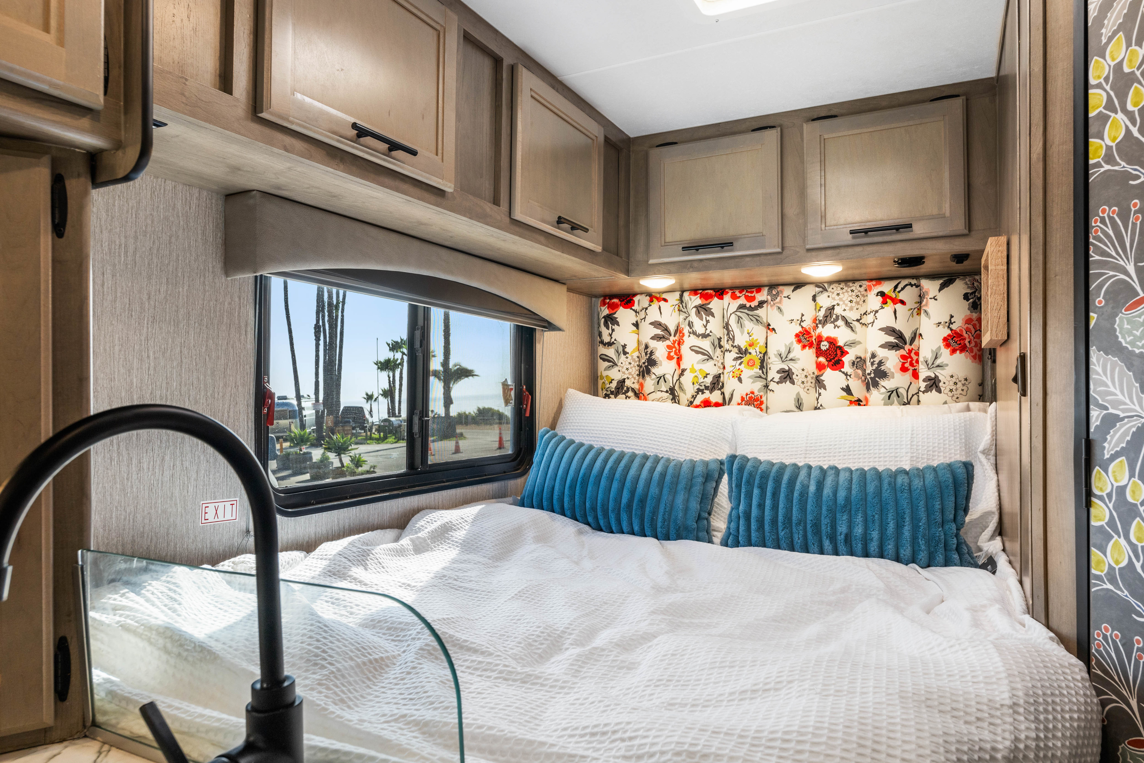 Inviting RV rental bedroom with a comfortable bed, vibrant floral headboard, and stunning coastal window view. Cozy mobile living.. COACHMEN Ford Transit 2022