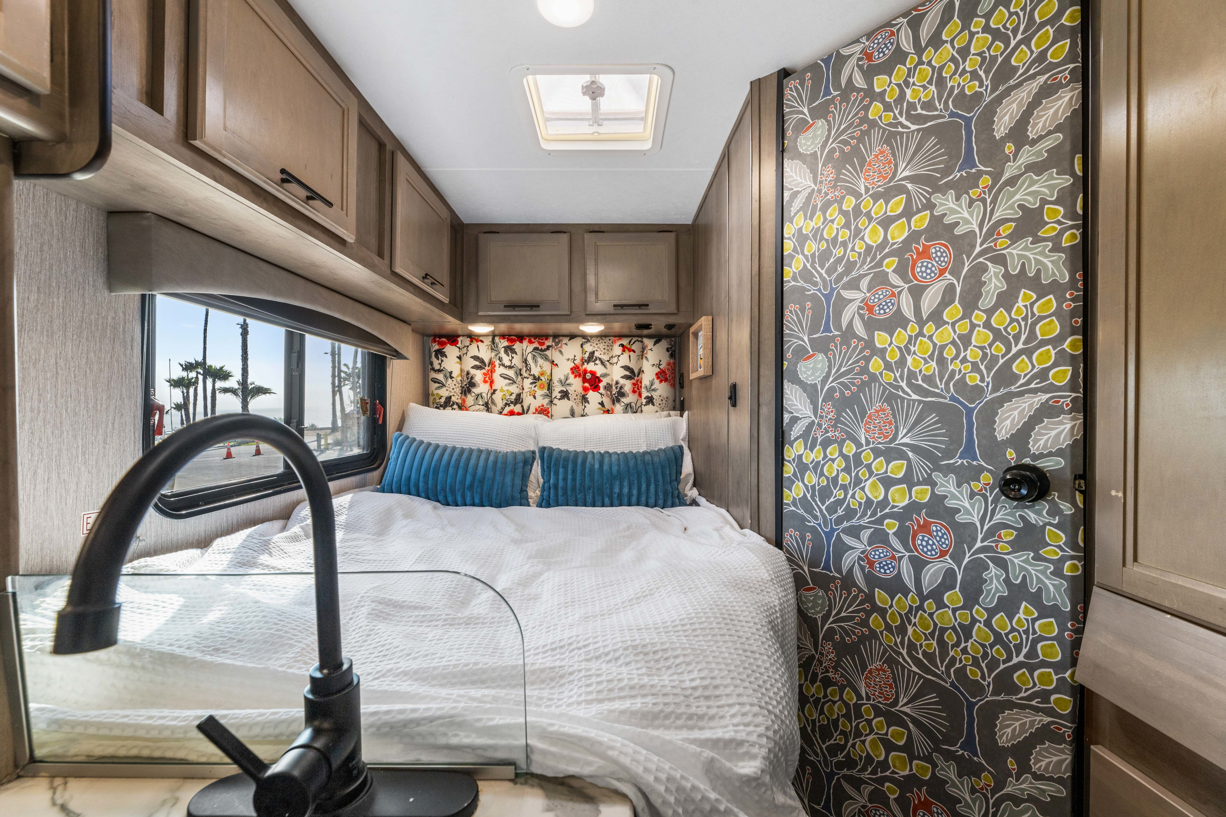 Cozy RV rental bedroom with modern decor, floral headboard, sink, and scenic ocean view through the window.. COACHMEN Ford Transit 2022