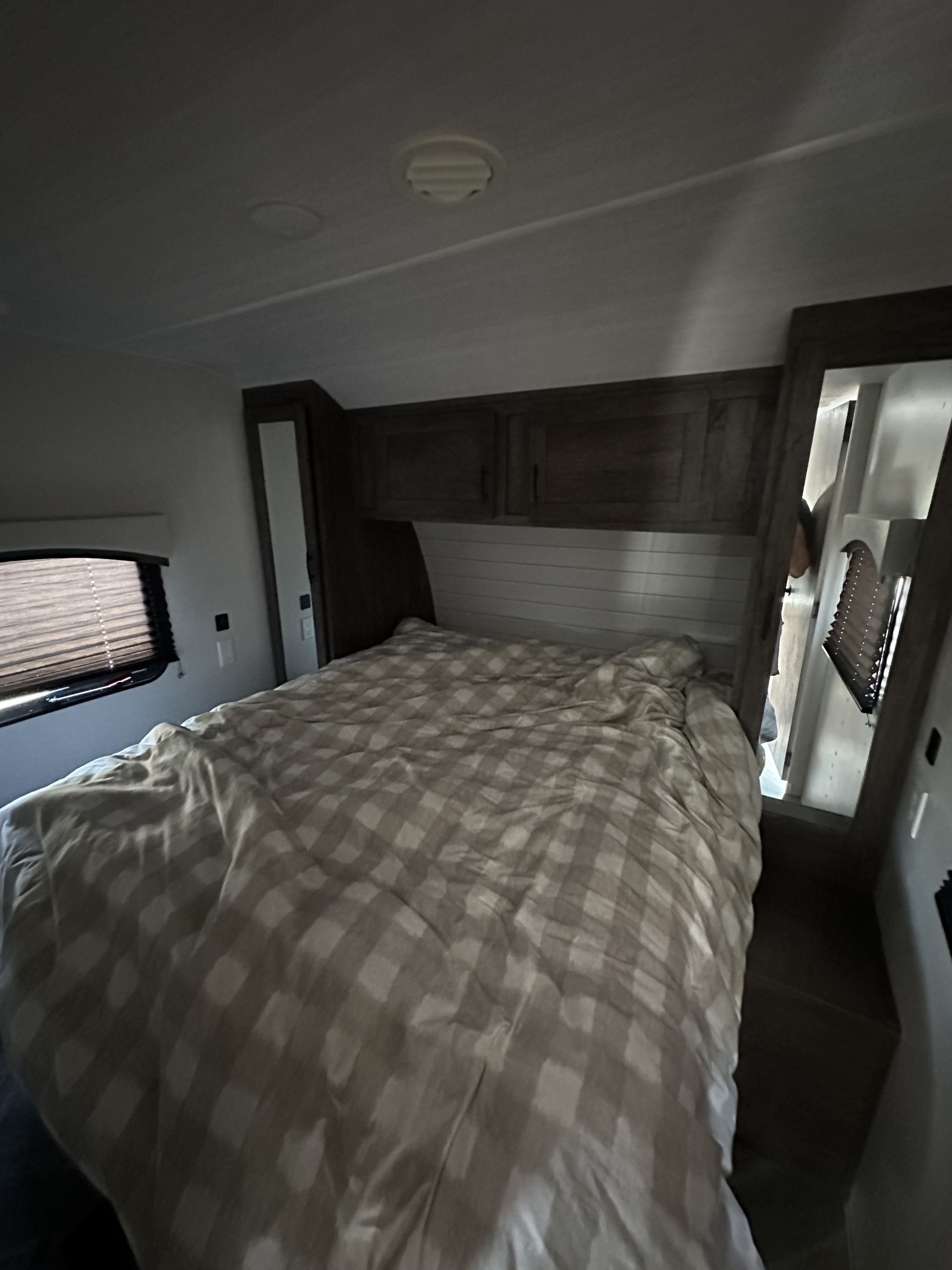 RV rental bedroom with a comfy, checkered bed, overhead storage cabinets, and window with blinds.. Forest River T2550 2021
