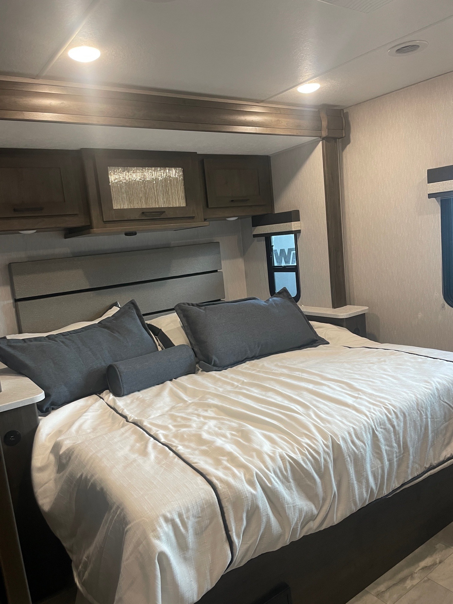 Cozy RV rental bedroom featuring a spacious bed with white linens, dark pillows, overhead cabinets, and a window. Ideal for travel.. Coachmen MIRADA 35ESF 2026