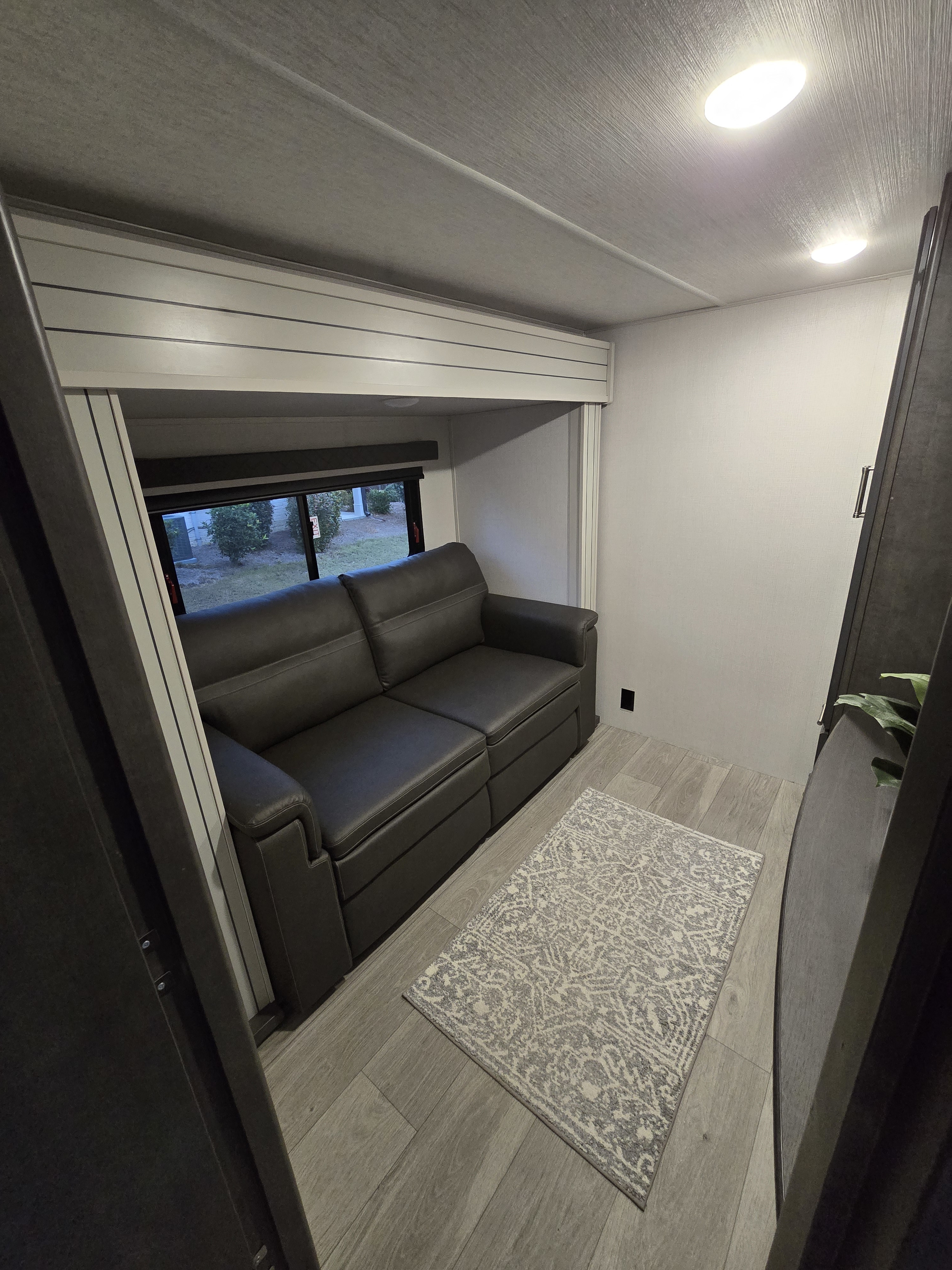 Cozy RV rental living area featuring a comfy sofa, window, and patterned rug on wood-look flooring.. Keystone RV Cougar 2024