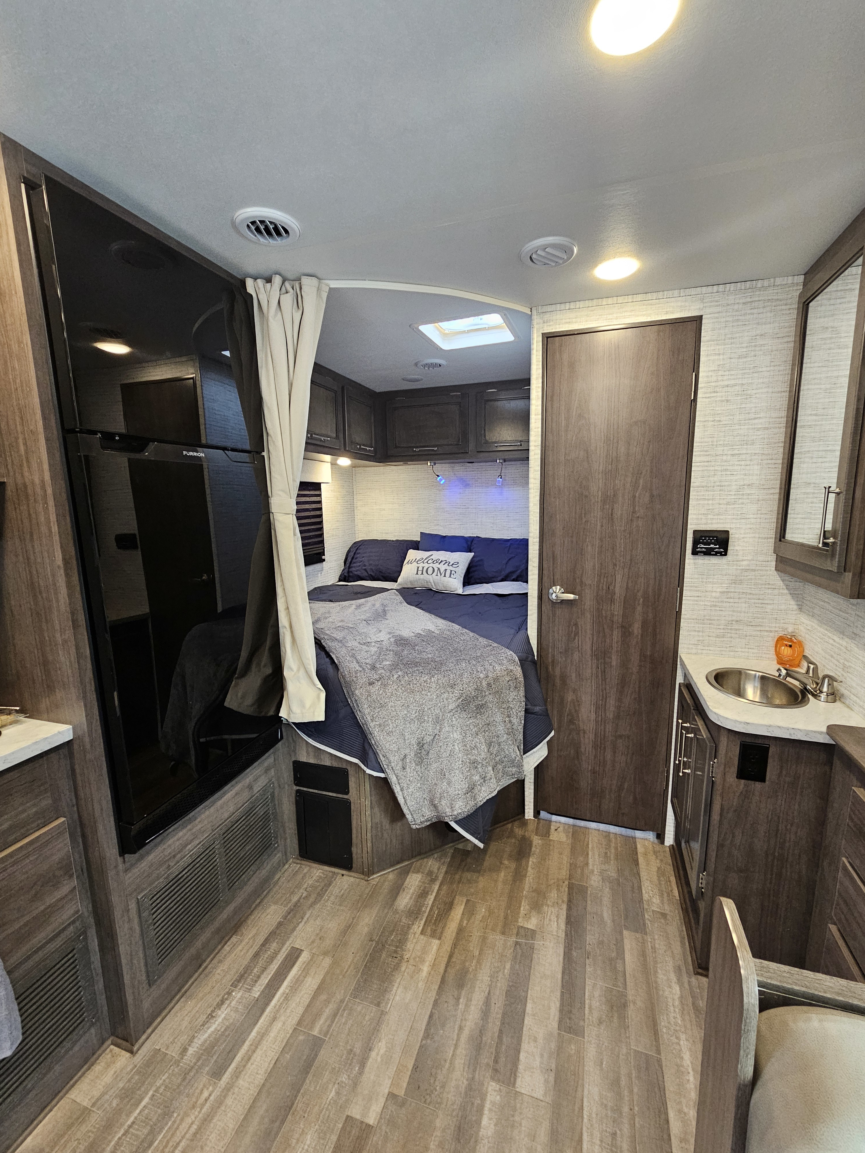 RV rental interior: cozy bedroom, a kitchenette with sink, large fridge, ample cabinets, and wood flooring.. Jayco Redhawlk SE 2025
