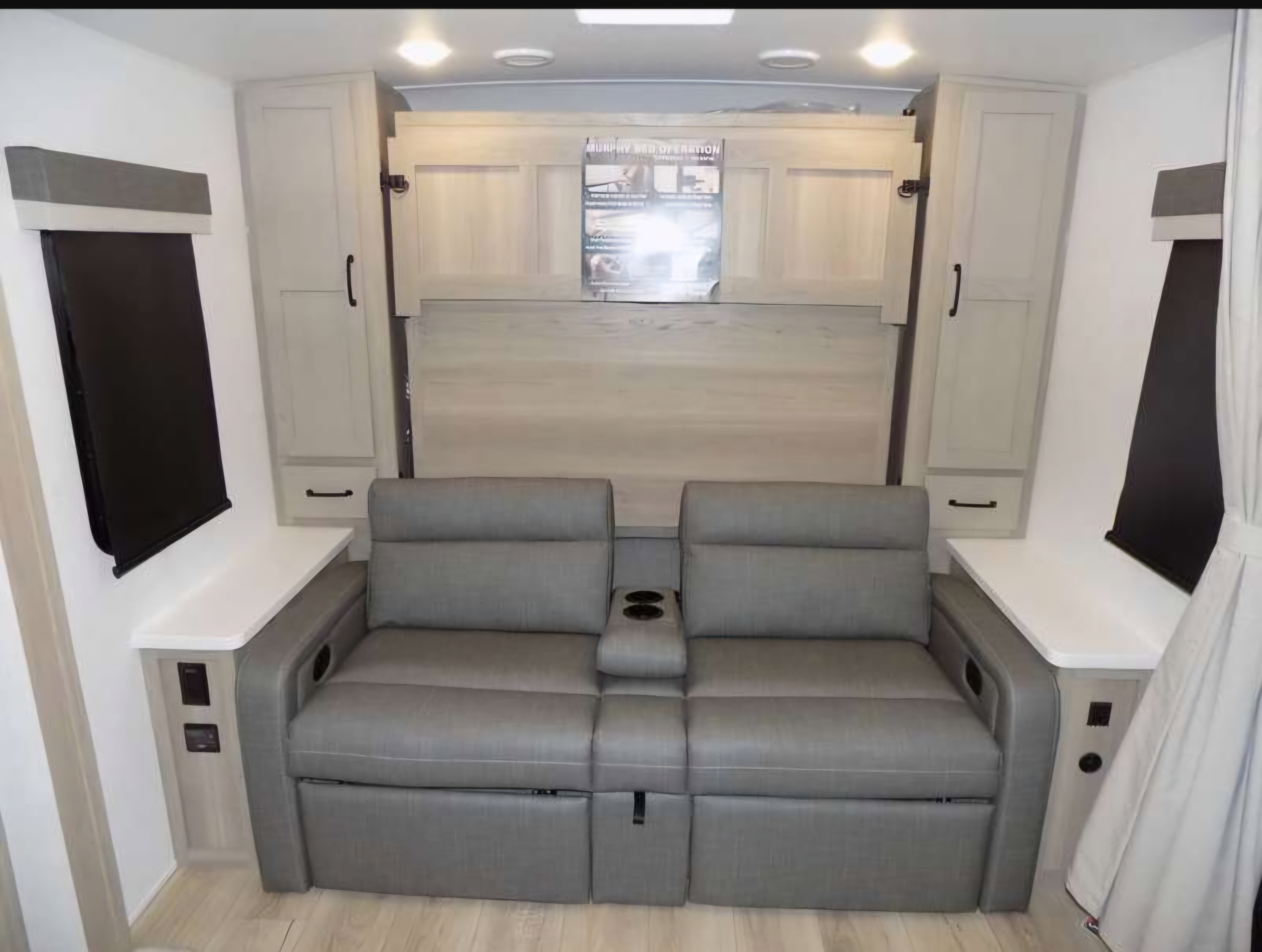 RV rental interior: two-seater reclining sofa with cupholders, flanked by cabinets and windows. Murphy bed is folded up.. Forest River Rockwood Mini Lite 2023