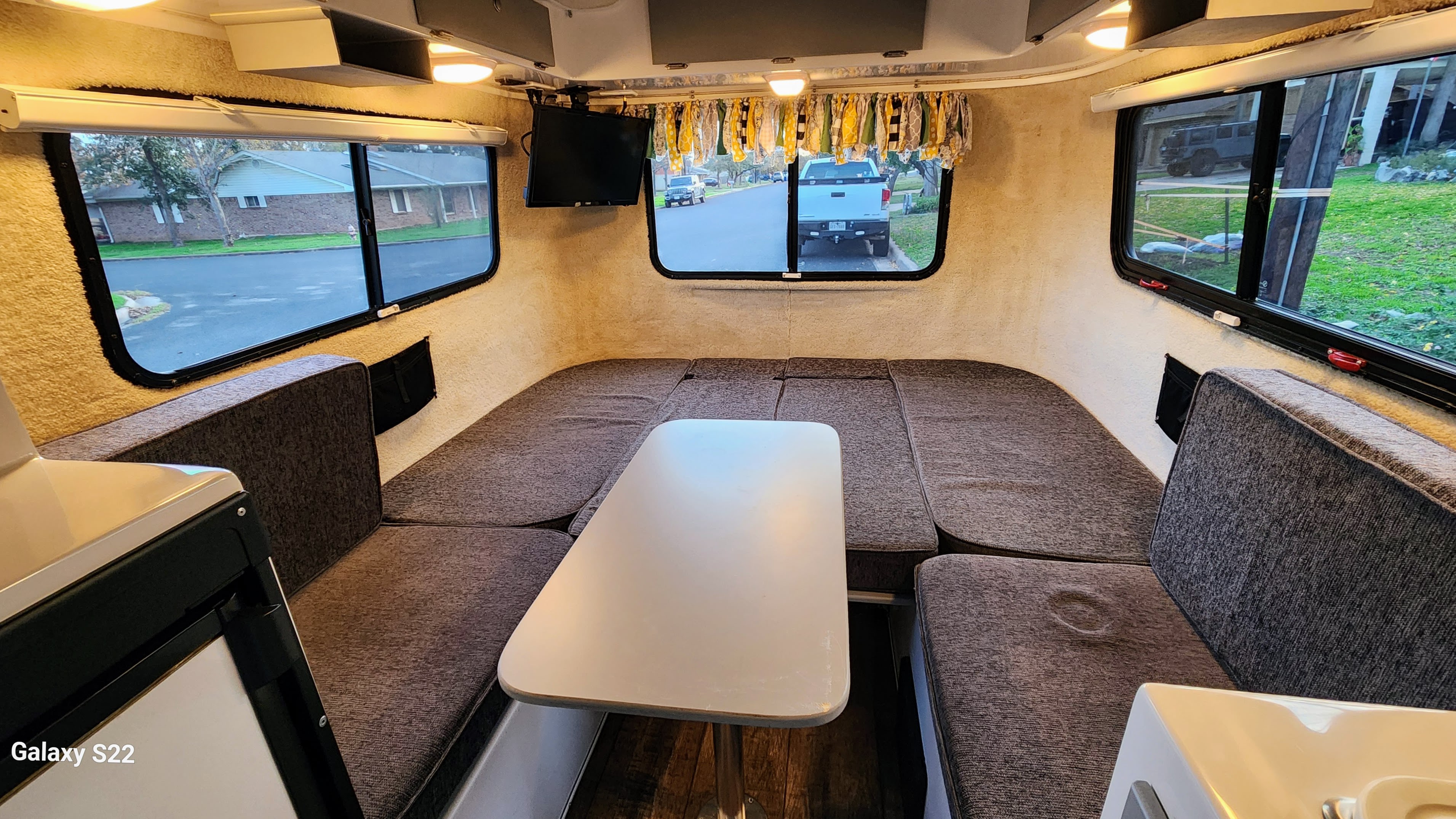 Cozy RV rental interior featuring a U-shaped dinette, convertible bed, and ample windows with street views.. Casita Casita Trailer 2019