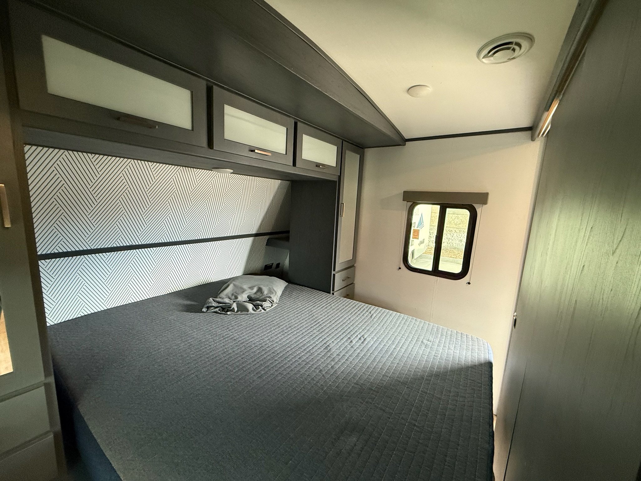 Inside an **RV rental**, a cozy bedroom features a gray quilted bed, patterned headboard, and ample overhead storage.. Keystone Bullet 2022