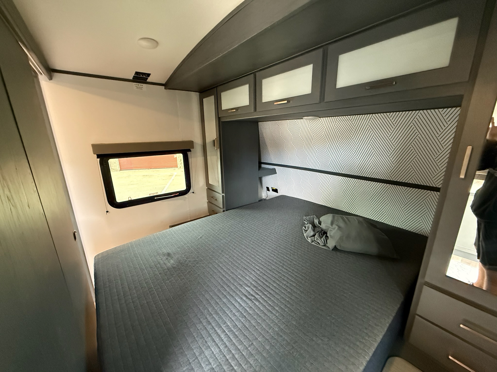 Comfortable RV rental bedroom featuring a grey quilted bed, modern overhead storage, and geometric wallpaper.. Keystone Bullet 2022