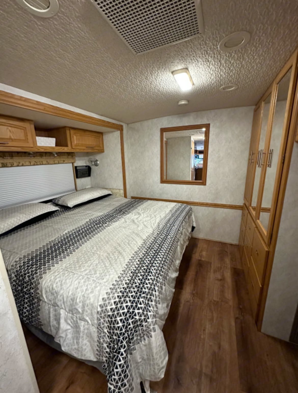Spacious RV rental bedroom with comfortable bed, overhead storage, mirrored wardrobe, and wood flooring, perfect for your travels.. Fleetwood Southwind 2004
