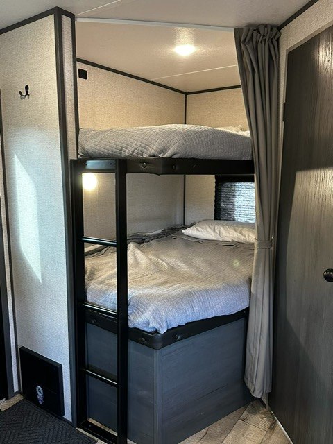 This RV rental features comfy bunk beds with grey covers and a ladder, perfect for families.. Dutchmen Aspen trail 2023