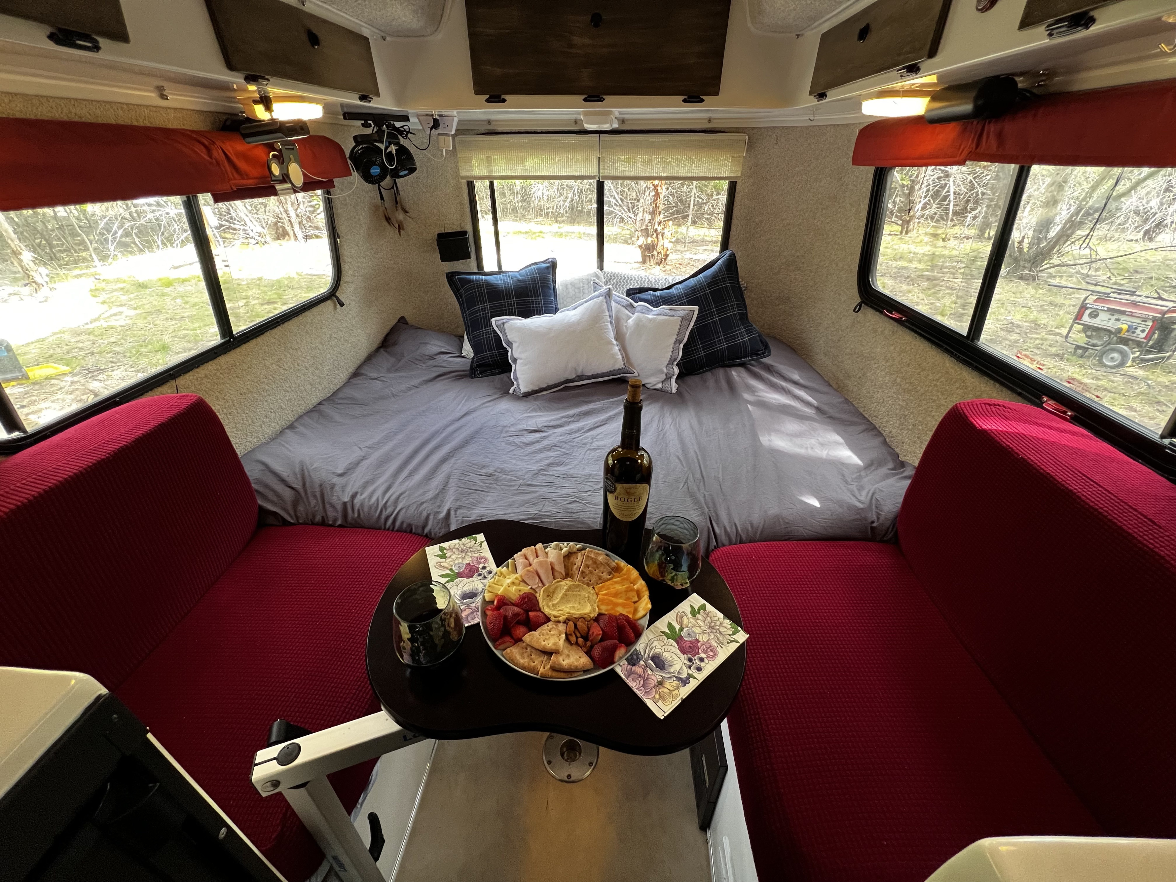 Cozy RV rental interior featuring a bed, red seating, and a charcuterie board with wine. Ideal for travel.. Casita Casita Trailer 2009