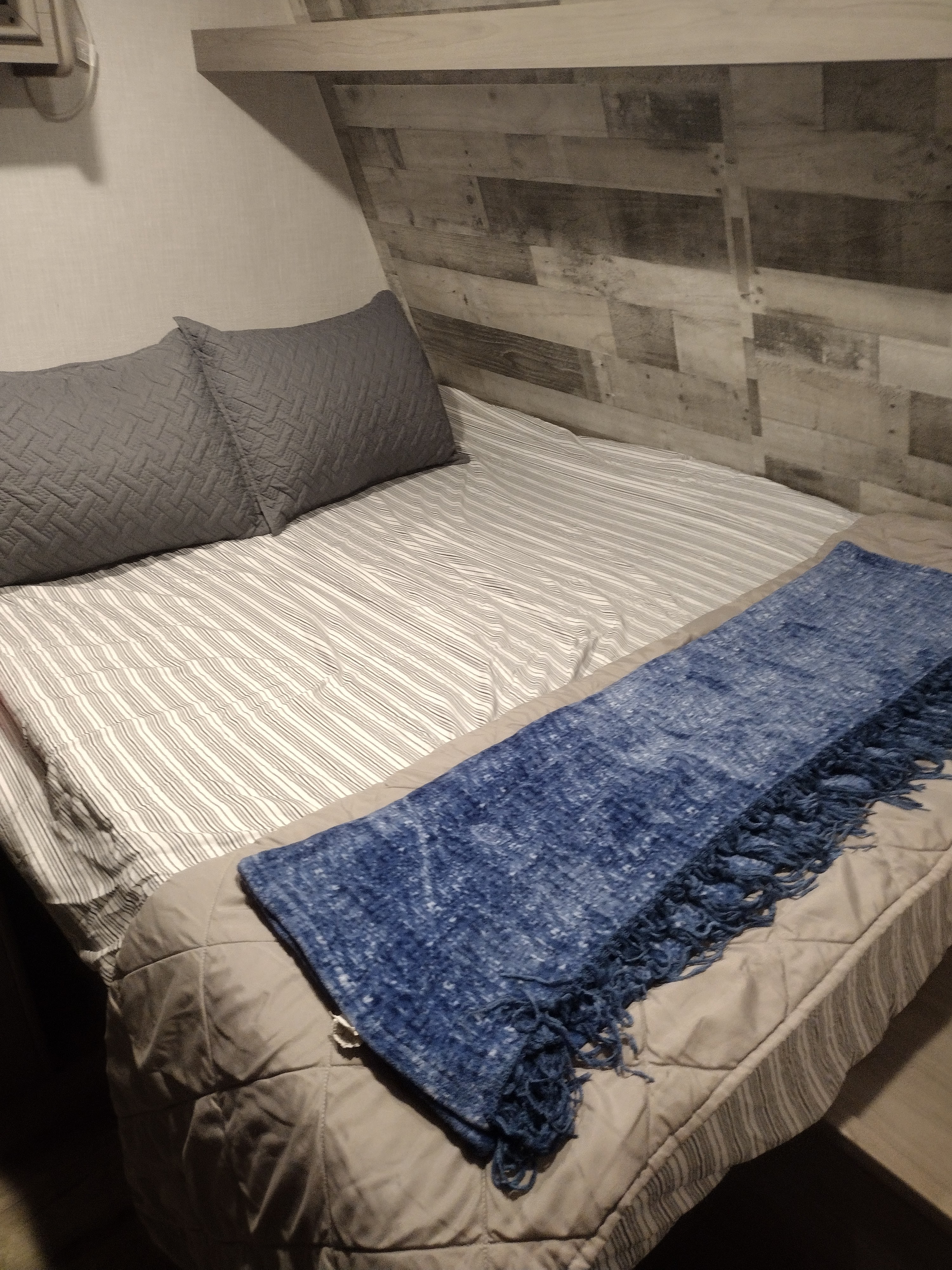 Cozy RV rental bed with quilted grey pillows, striped sheets, and a blue blanket.. Coleman Lantern 2023