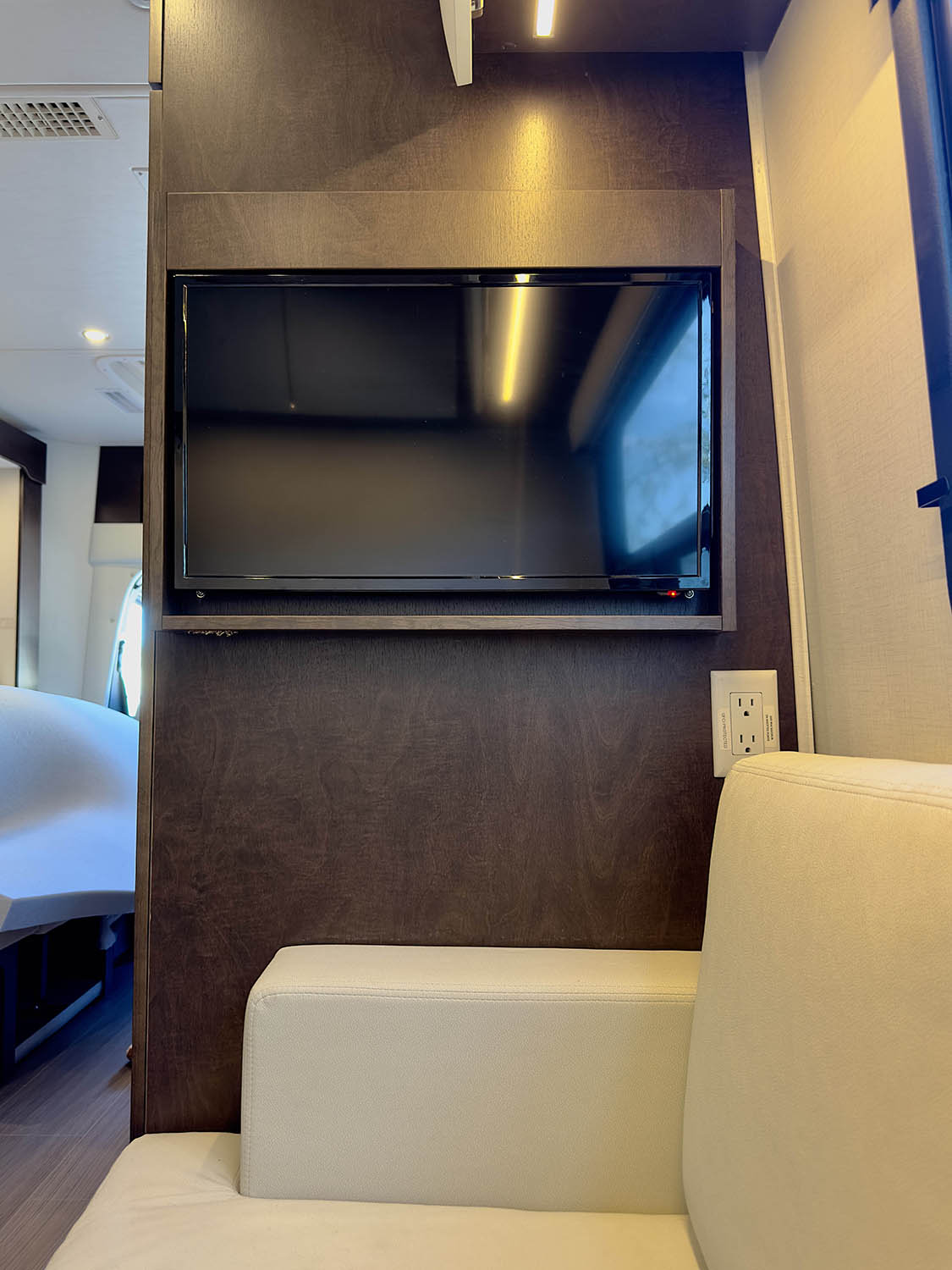 Compact RV rental interior with wall-mounted TV, light sofa, and power outlet. Functional living space for travel.. Leisure Travel Vans Unity 2022