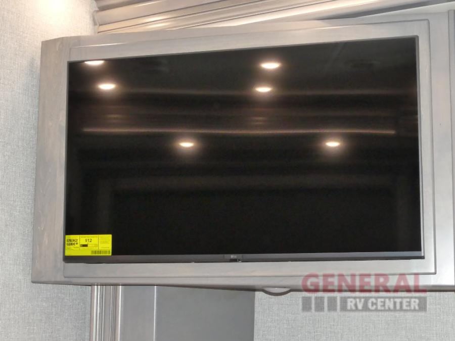 Enjoy comfortable living with a mounted TV in this RV rental. Reflections of overhead lights are visible on screen.. Holiday Rambler Armada 2024
