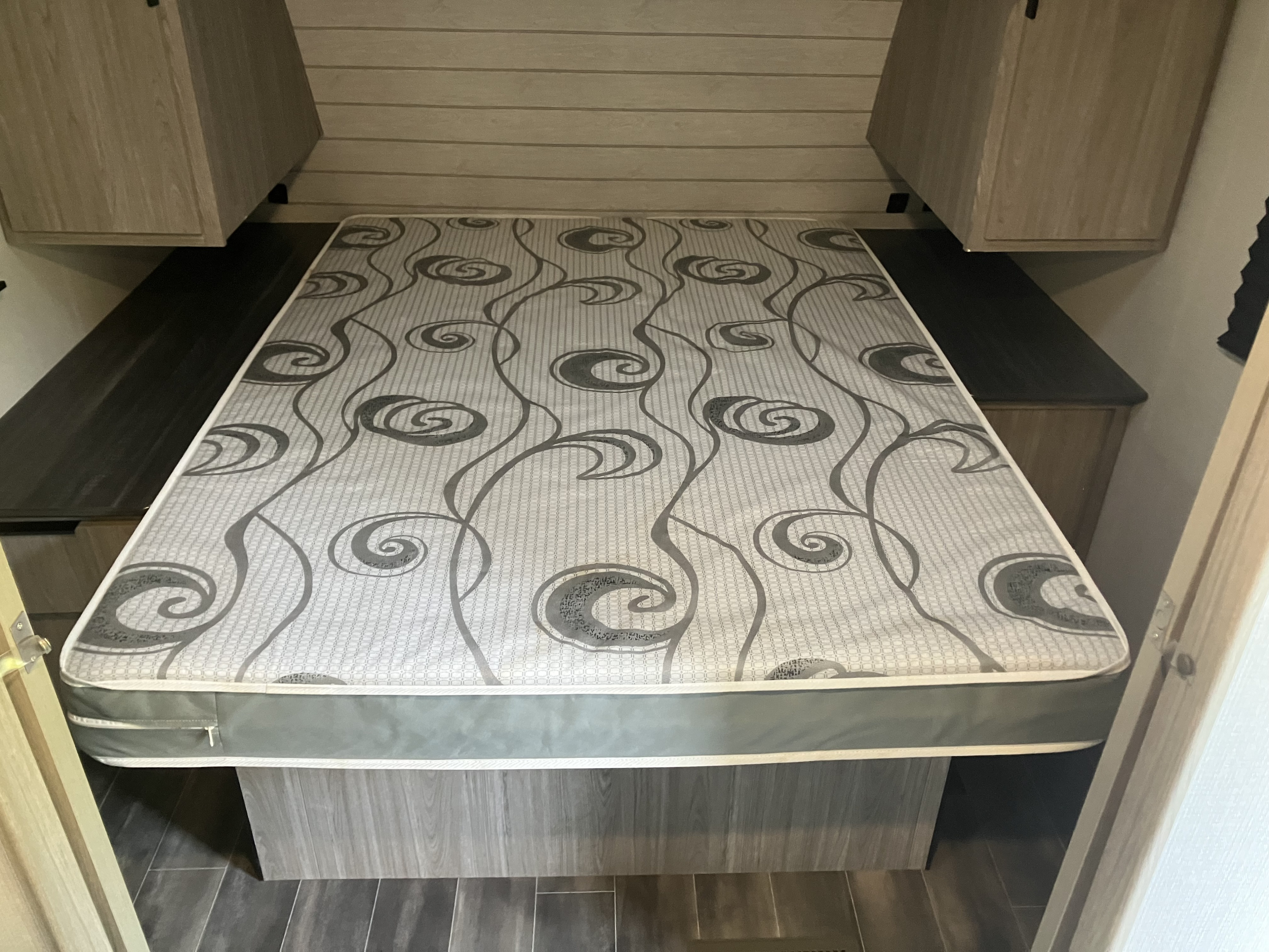 This RV rental shows a compact sleeping area with a patterned mattress, surrounded by built-in storage and overhead cabinets.. Keystone RV Passport SL 2021