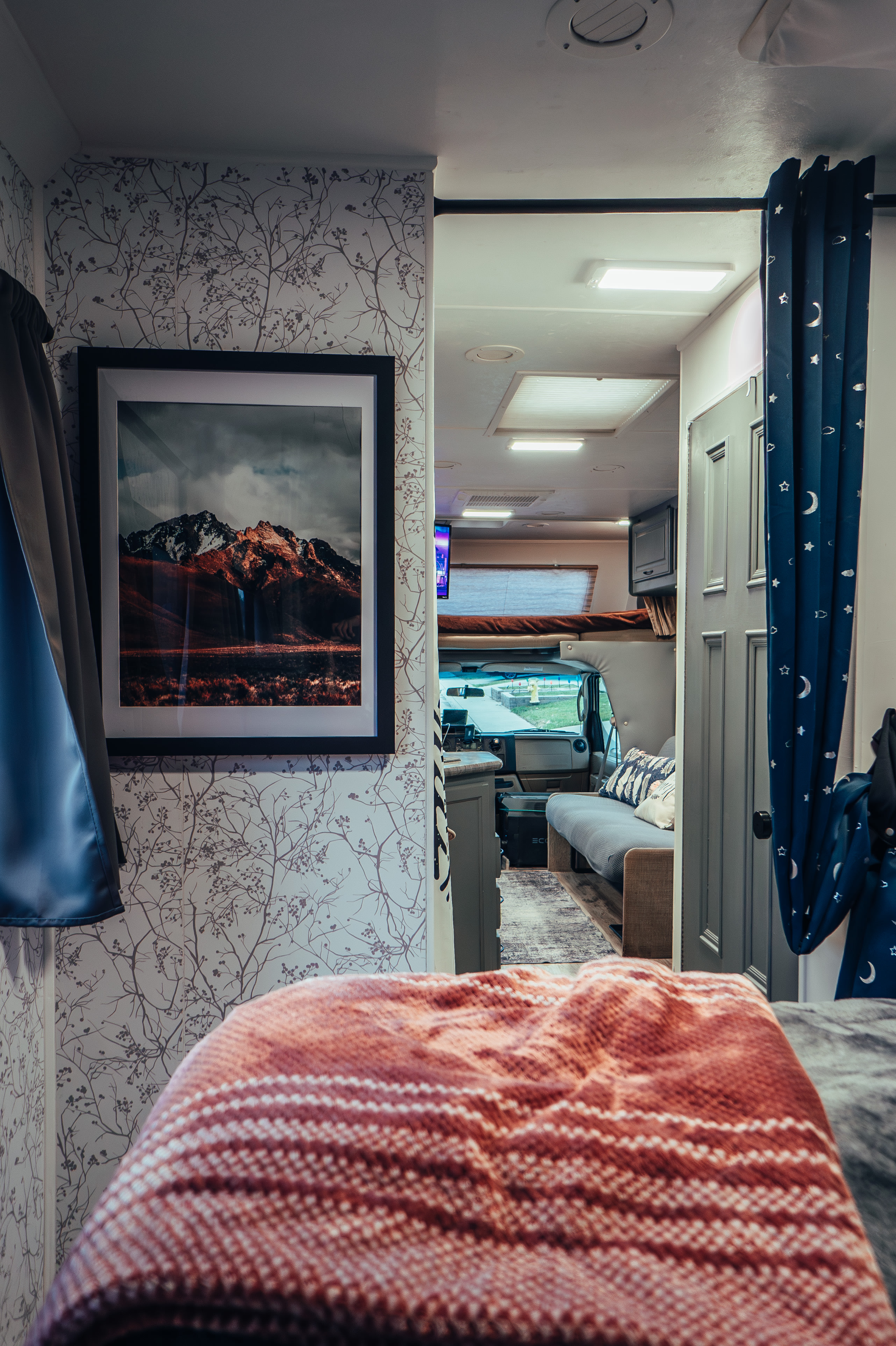 Experience comfort in this RV rental! Cozy bedroom, framed mountain art, and blue curtains leading to the living area and cockpit.. Four Winds Four Winds Motorhome 2011