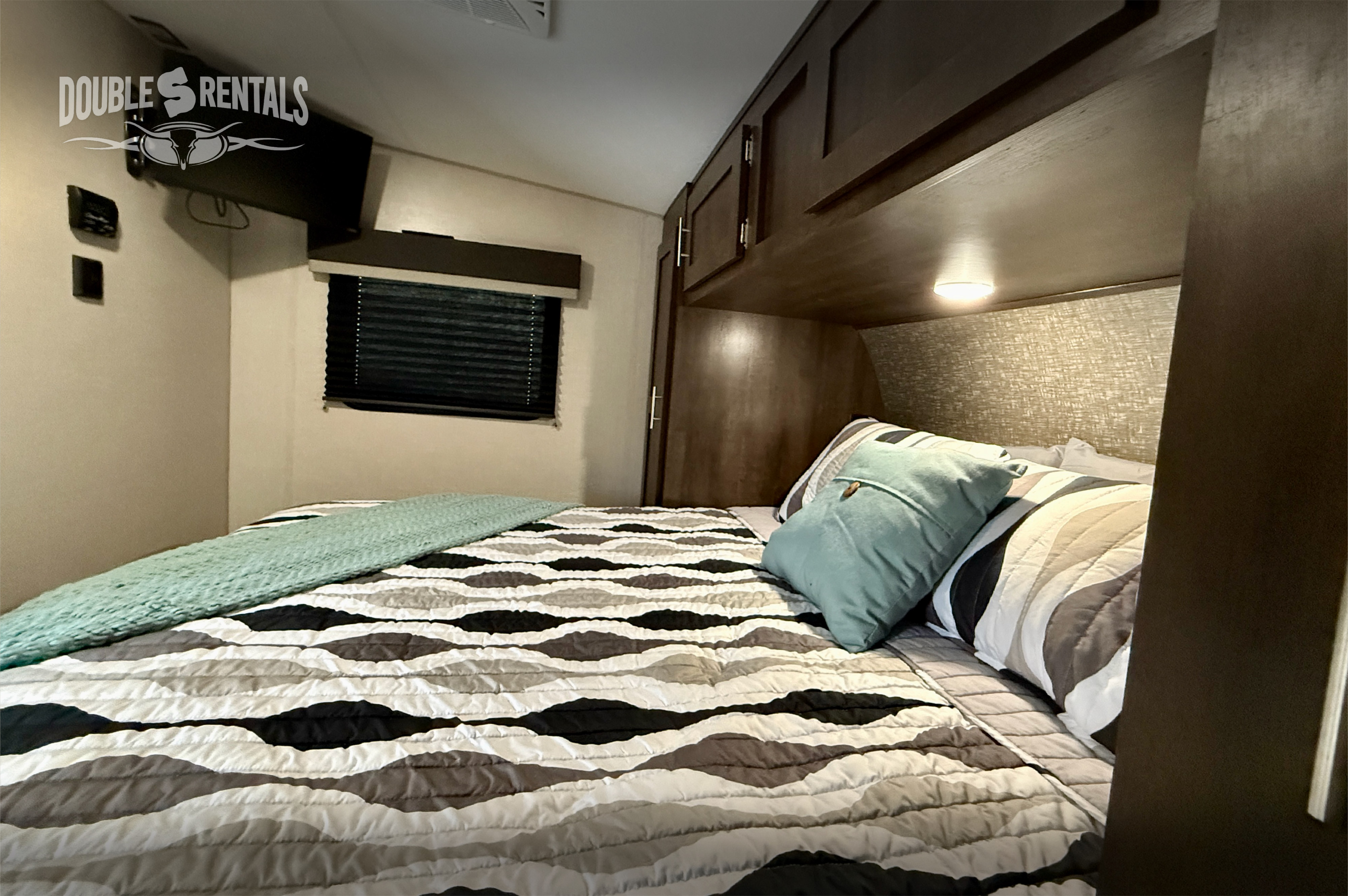 Explore comfort in this RV rental bedroom, featuring a cozy bed with patterned bedding, overhead storage, and a TV.. KZ Sportster 2021