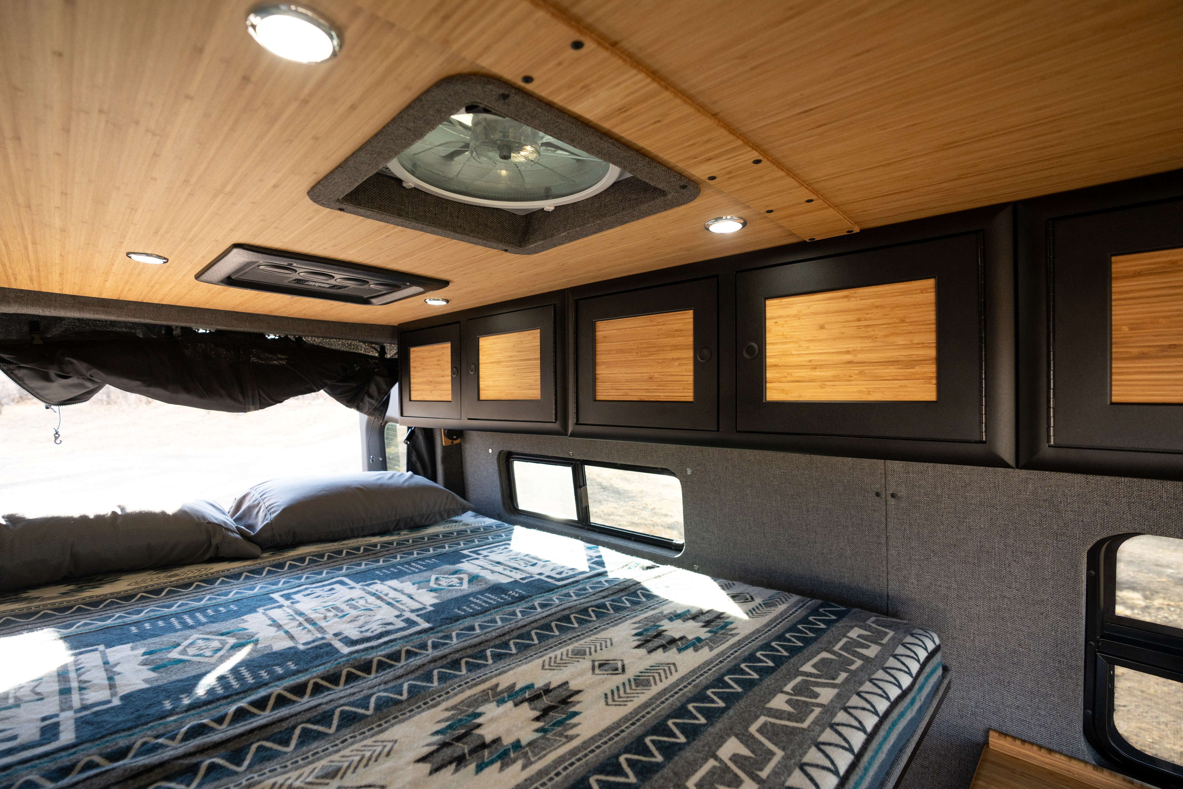 Comfortable RV rental interior featuring a bed, wood-paneled ceiling, and dark cabinets with light bamboo doors.. Mercedes-Benz Sprinter 2024