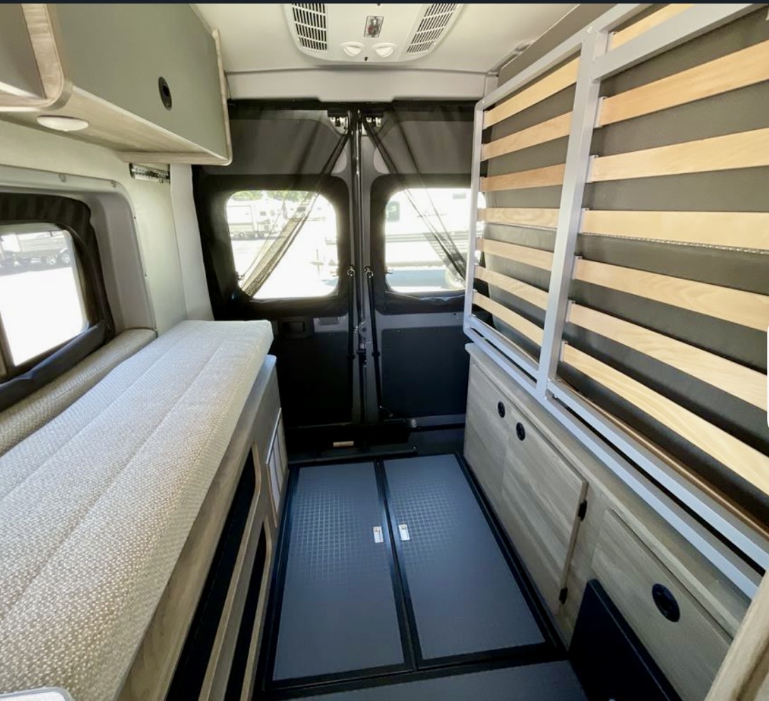 This RV rental interior shows a compact camper van. Features include a comfy bed, integrated storage, and a vertical slat bed frame.. solis 59px 2025