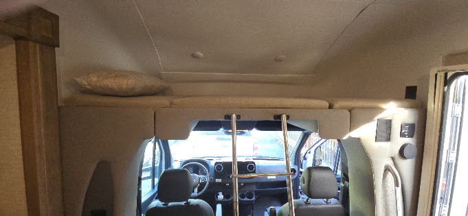 Inside an rv rental, featuring a comfortable over-cab bunk bed with ladder, overlooking the driver's area. Road trip ready!. Tiffin Wayfarer 2023