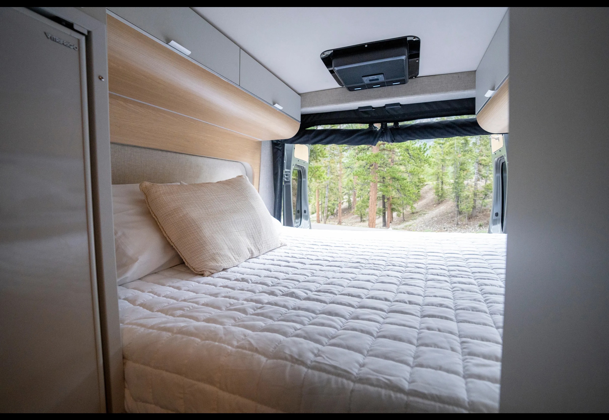 Cozy RV rental bedroom with a comfy bed and a beautiful forest view through the open rear doors.. Noovo Pop 2024