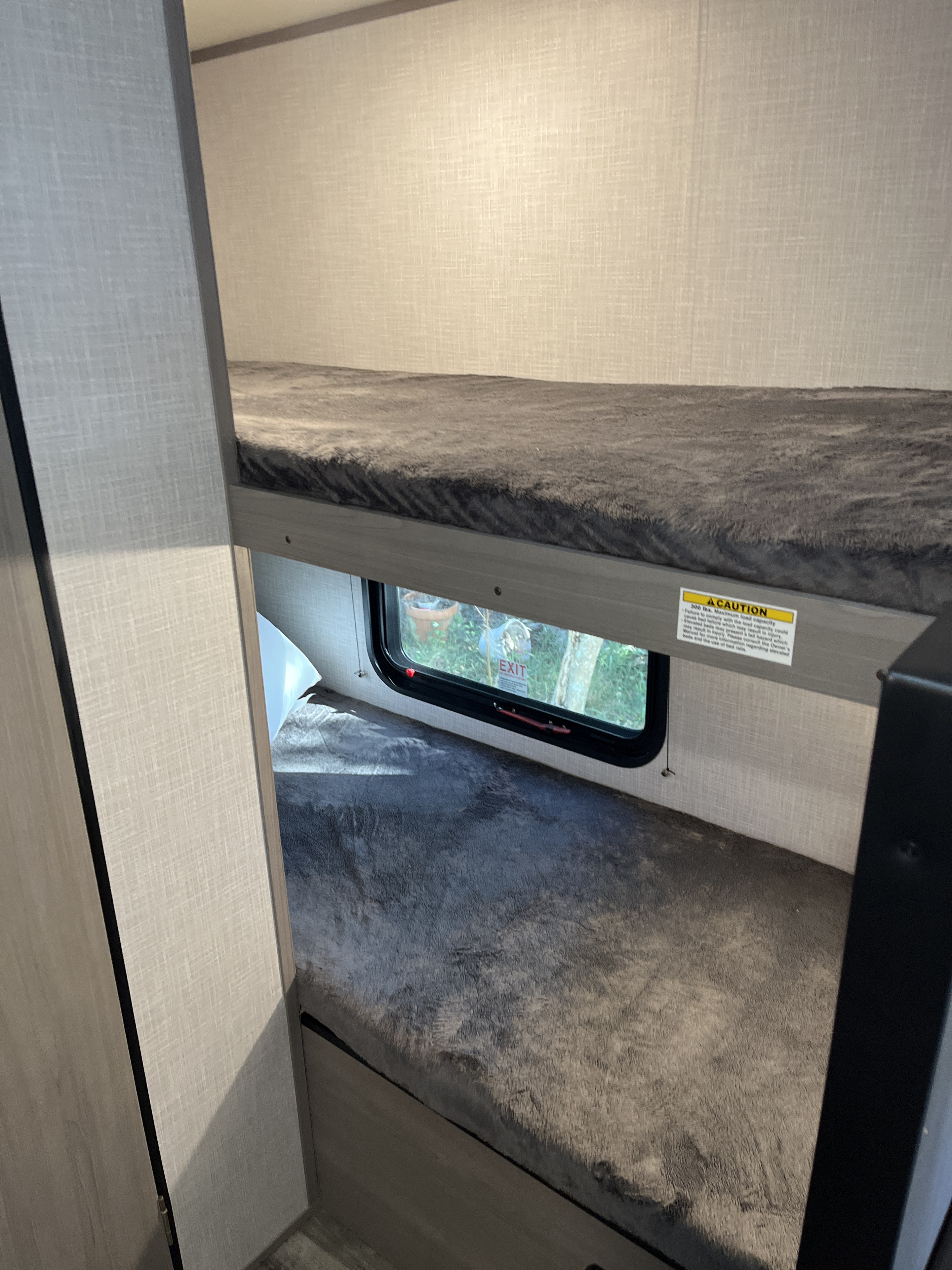 Inside an RV rental: Two plush bunk beds with a window, emergency exit, and safety caution label for travel.. Coachmen 17b 2023