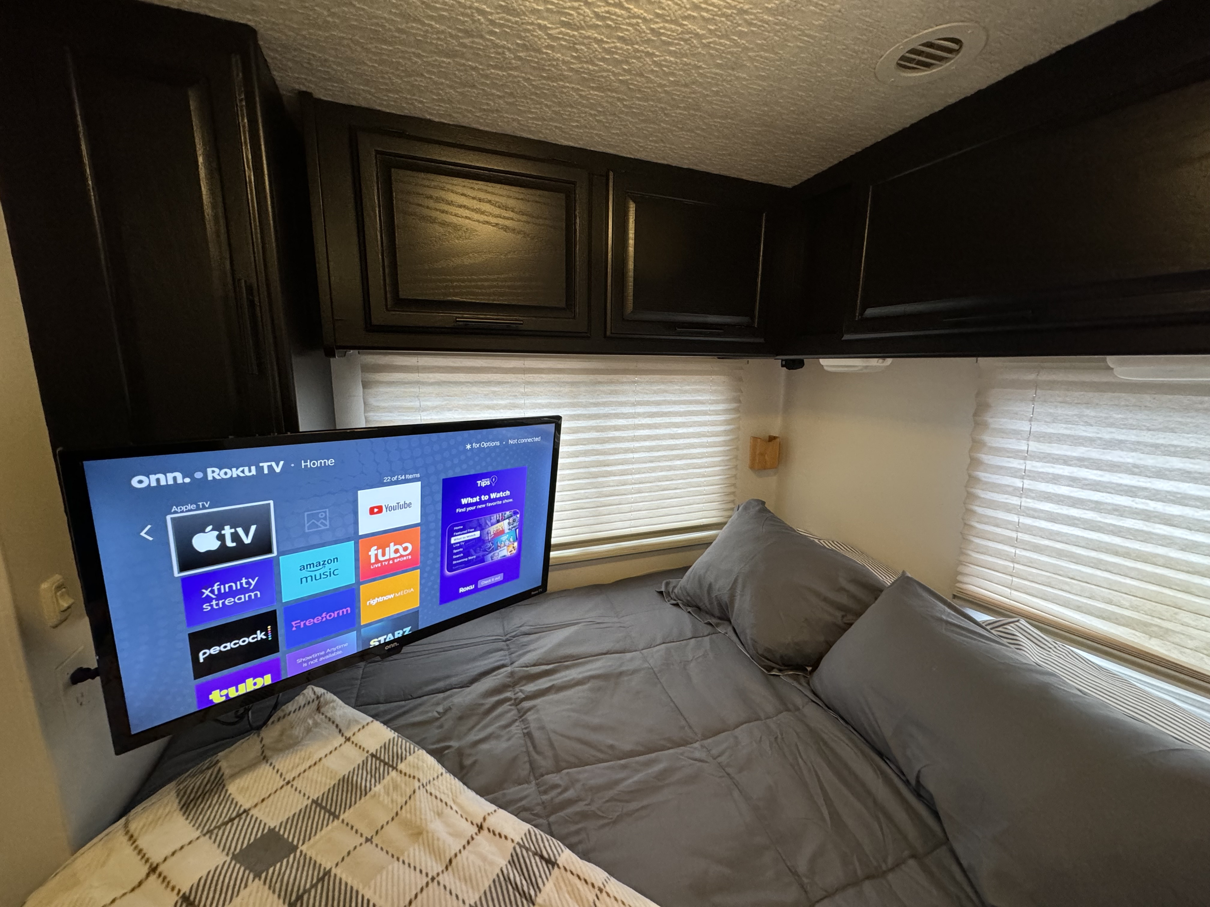 Cozy RV rental bedroom with a comfortable bed, overhead cabinets, and a Roku TV displaying streaming services.. Winnebago Minnie 2002