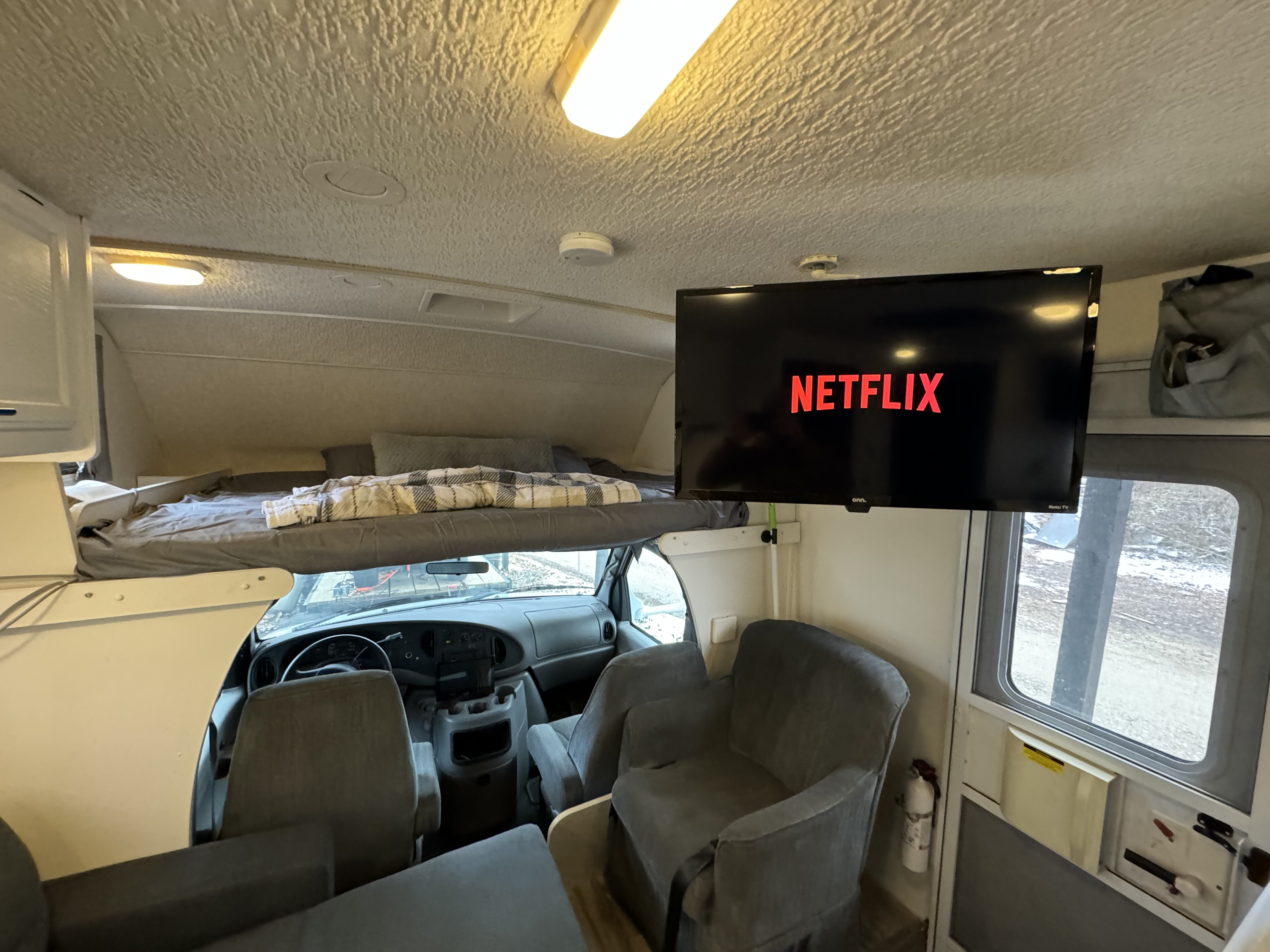 Cozy RV rental interior: overhead bed, Netflix TV, & seating. Perfect for a comfortable road trip experience.. Winnebago Minnie 2002