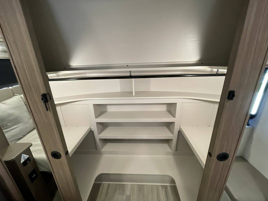 Compact sleeping and storage area in an RV rental, with built-in white shelves and a top black hanging rod.. Alliance RV Paradigm 2024