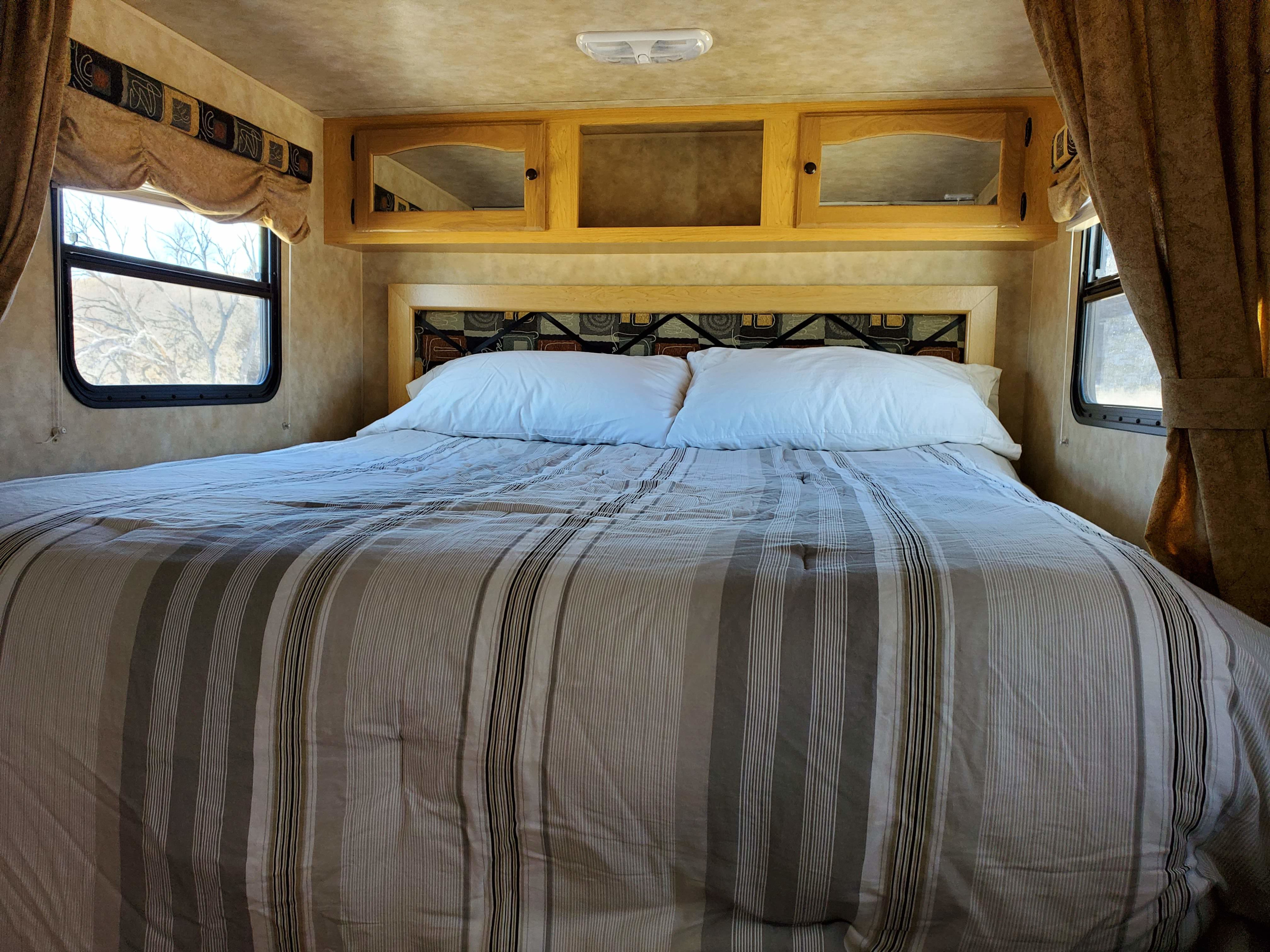 Cozy RV rental bedroom displaying striped bedding, a patterned headboard, and useful overhead storage with mirrored cabinets.. K-Z Manufacturing Spree Super-Lite 2009