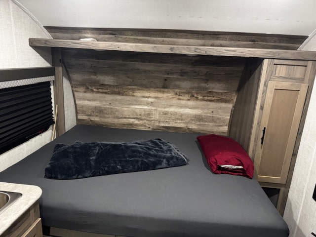 Compact RV rental bedroom with a bed, wood headboard, window, and storage cabinet for comfortable travel.. Gulf Stream Kinsport Super Lite 2022