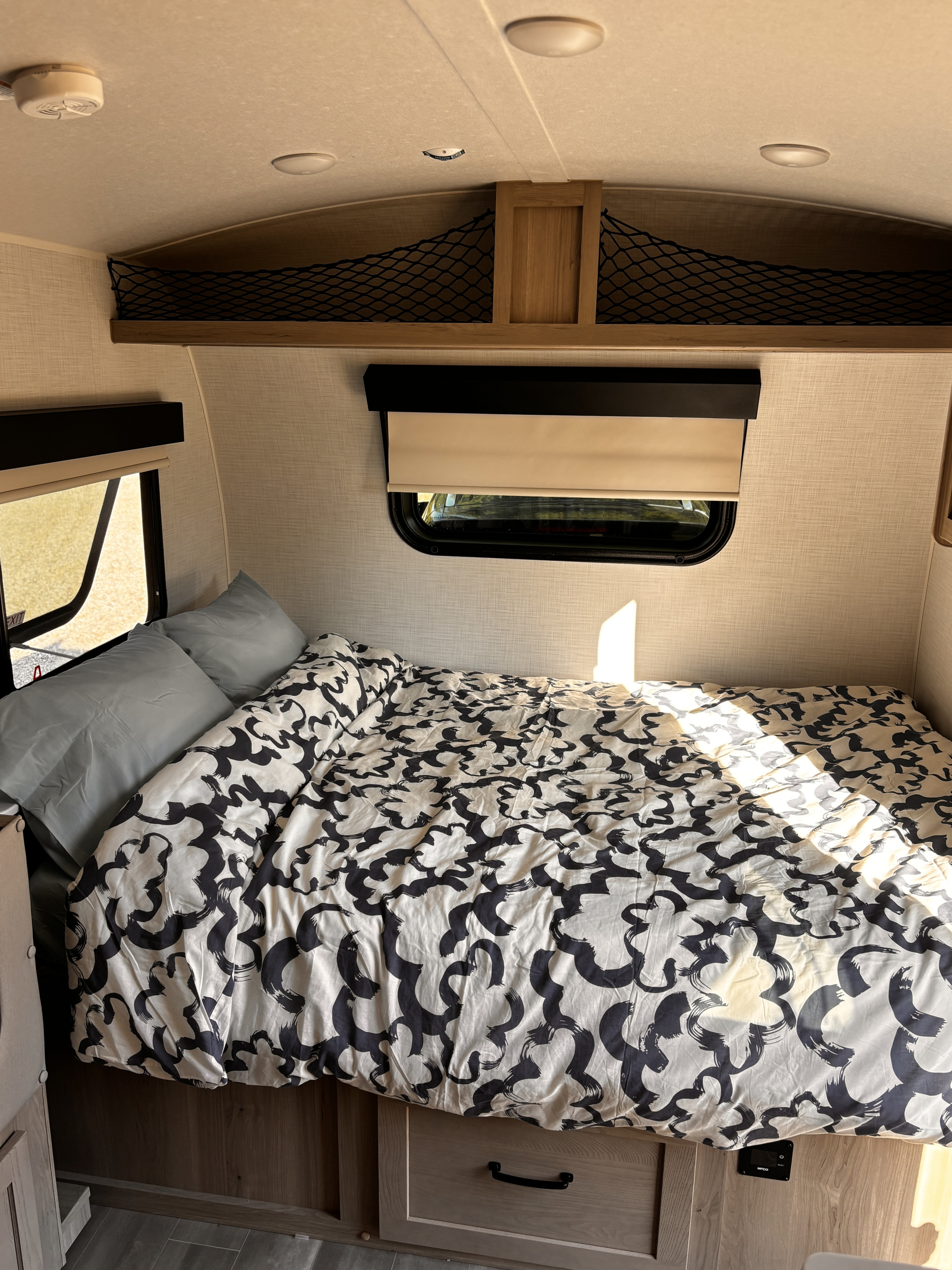Comfortable RV rental bed featuring a unique patterned duvet, window, and practical overhead storage nets.. Forest River Rockwood Geo Pro 2024