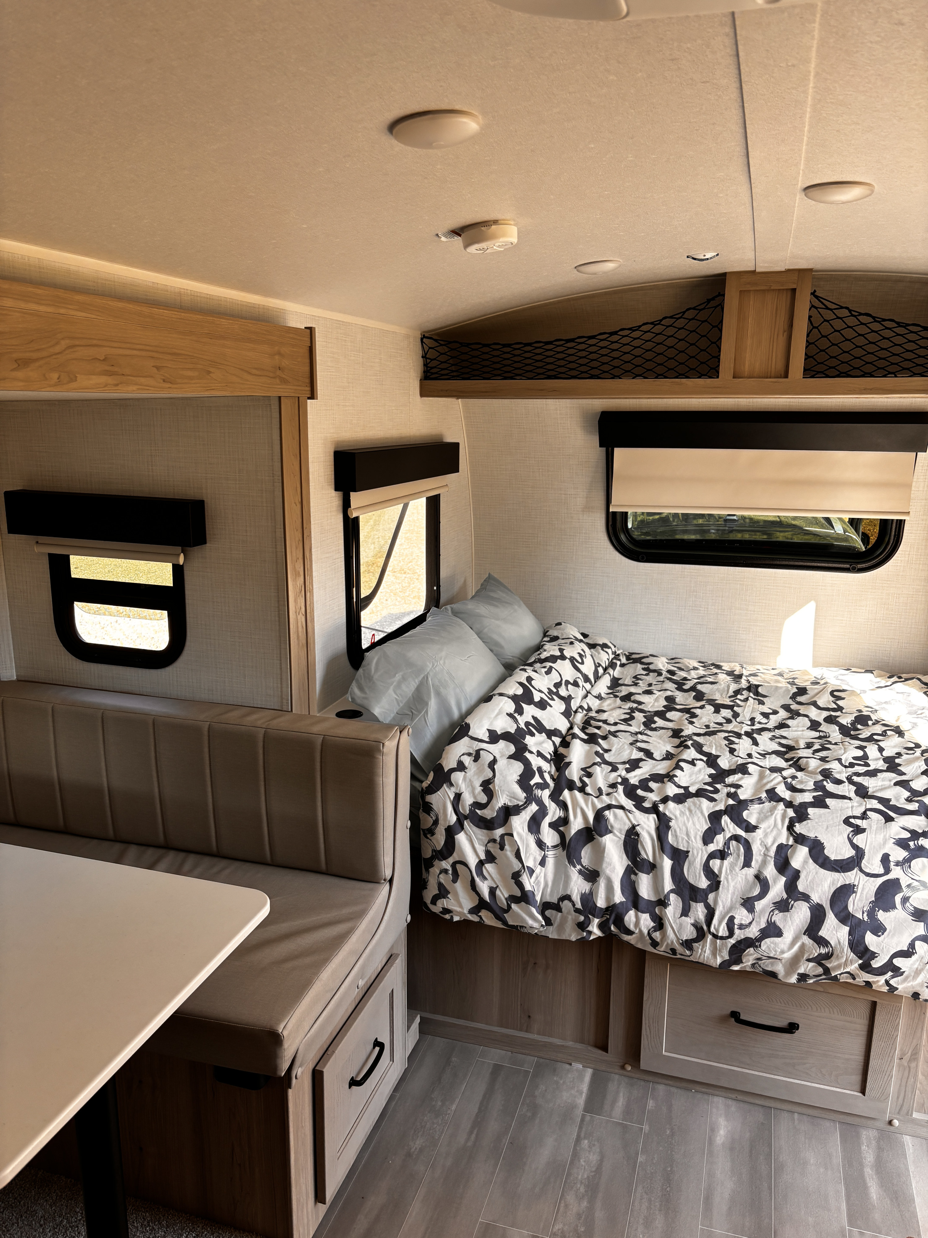 An RV rental interior showing a comfortable bed, dinette seating, and bright windows with light wood trim.. Forest River Rockwood Geo Pro 2024