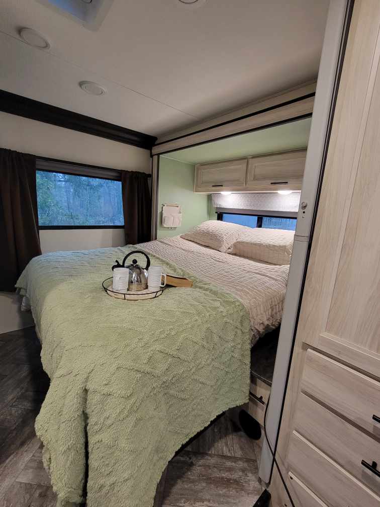 Cozy RV bedroom perfect for your RV rental getaway. Features a comfy bed, overhead storage, and window views.. Forester LE 2022