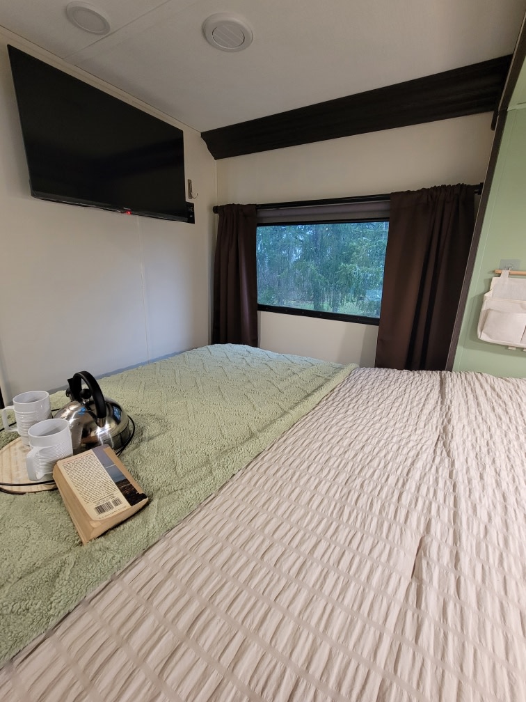 RV rental bedroom with two sleeping areas, a wall-mounted TV, forest view, plus a kettle & book.. Forester LE 2022