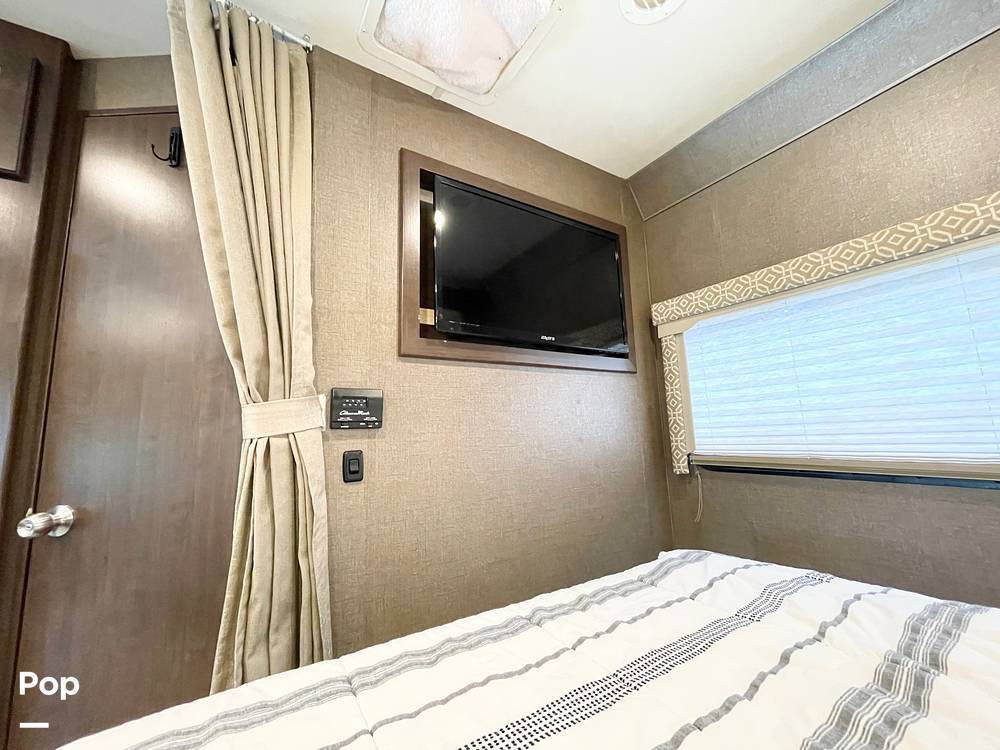 Inside an RV rental bedroom: bed with striped bedding, wall TV, window with blinds, and privacy curtain.. Thor Freedom Elite 2018