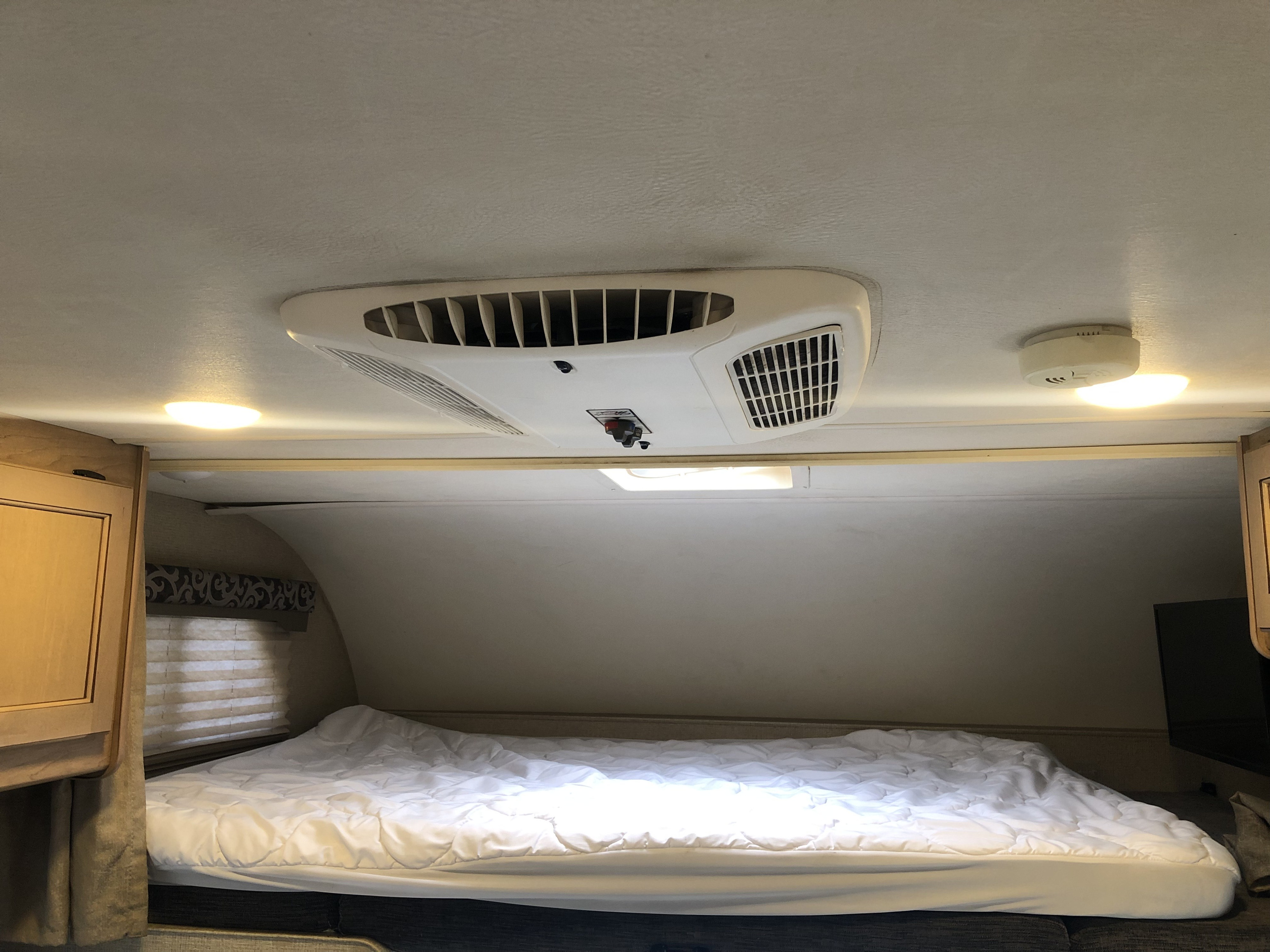 Cozy RV rental bedroom with a large bed, air conditioner, and bright ceiling lights, perfect for travel.. Thor Four Winds 2019