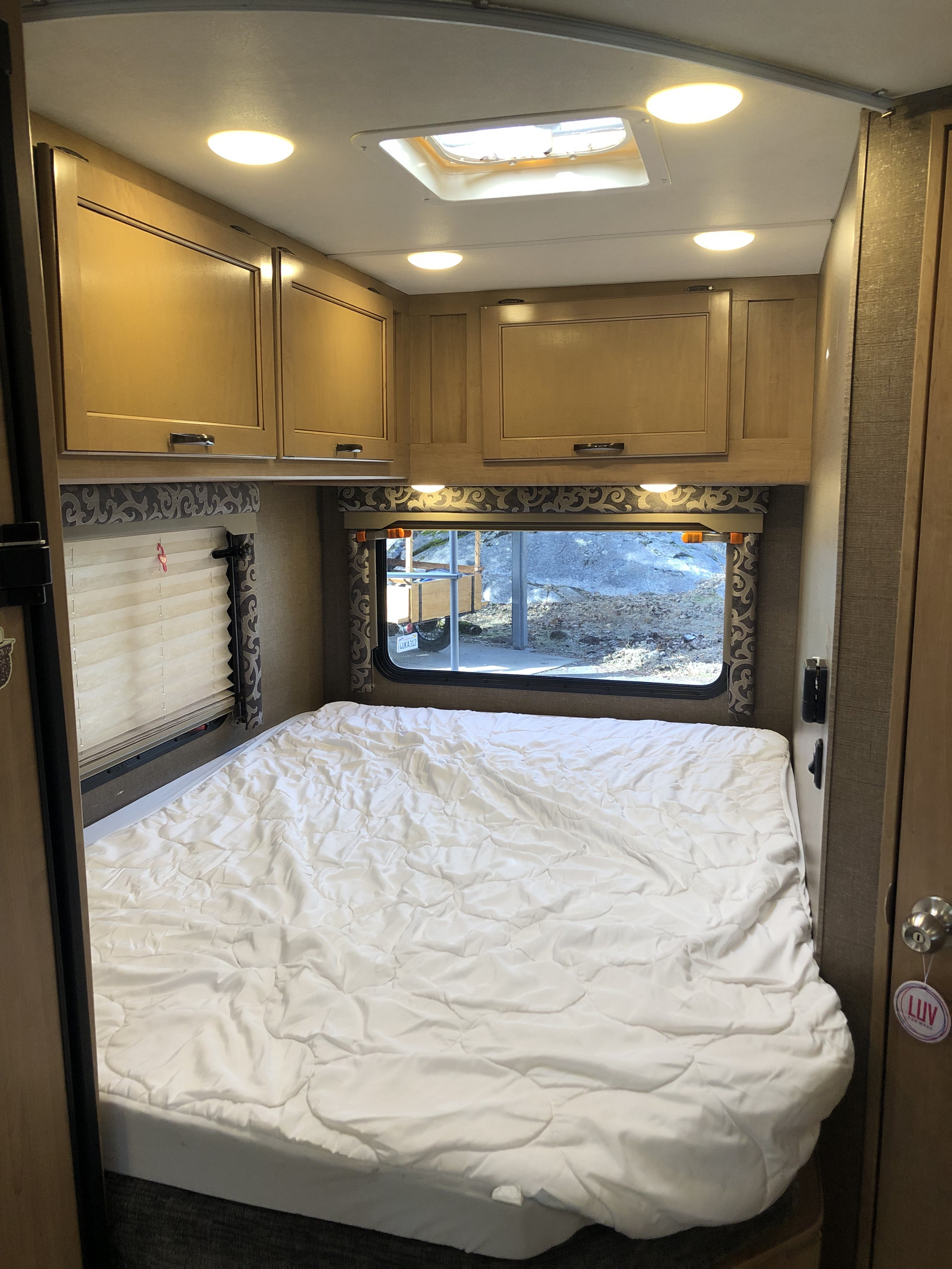 RV rental bedroom interior: cozy space with white bed, skylight, overhead cabinets, and window view.. Thor Four Winds 2019