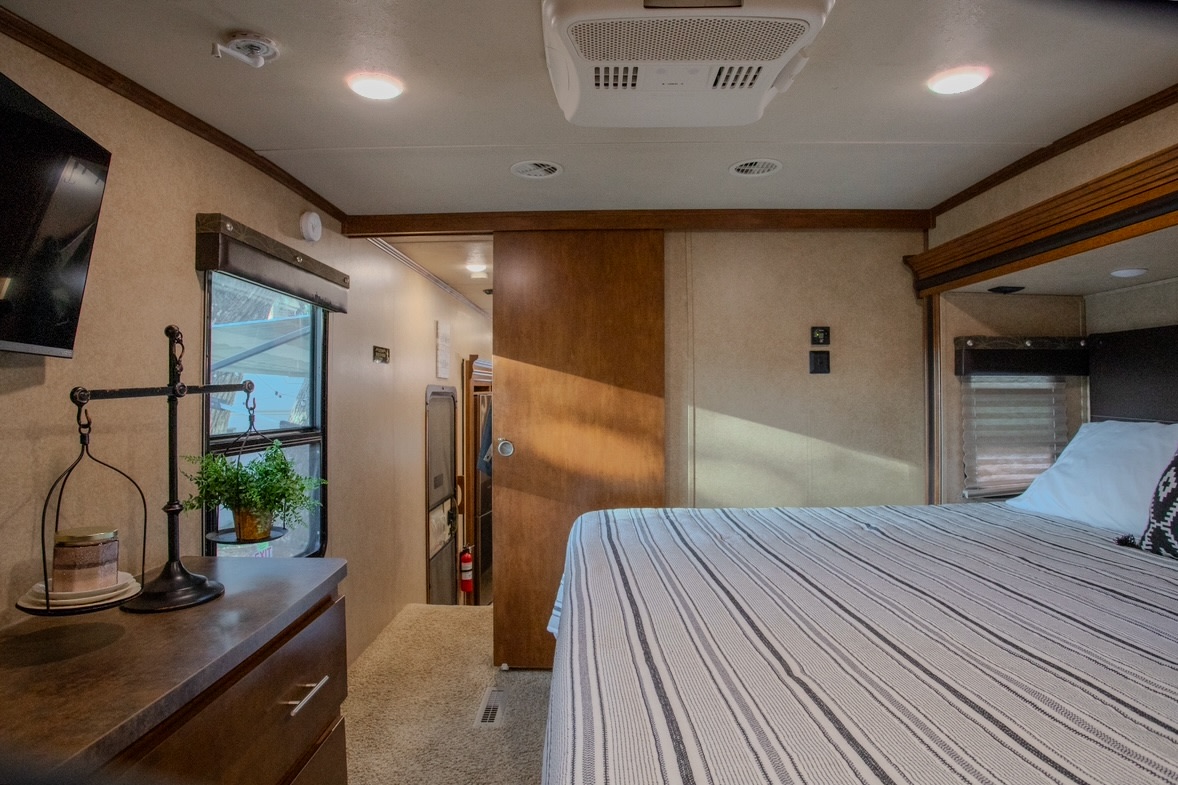 Spacious RV rental bedroom featuring a striped bed, dresser, window, and connecting living area. Ideal for comfortable travel.. Forest River XLR Thunderbolt Toy Hauler 2014