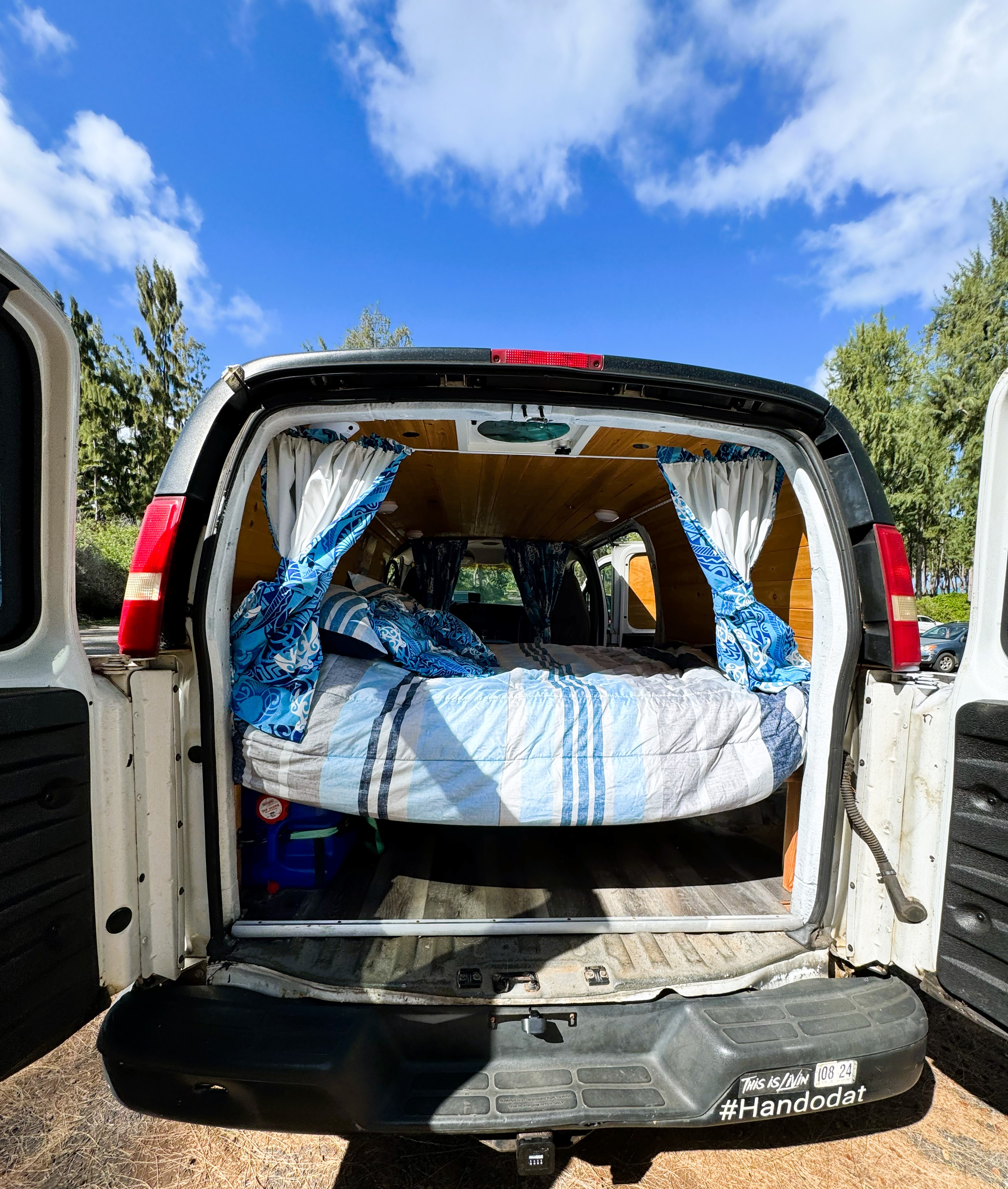 Open back of a white camper van reveals a cozy bed and wood paneling, great for vanlife adventures or an RV rental.. Chevrolet Express 2500 2004
