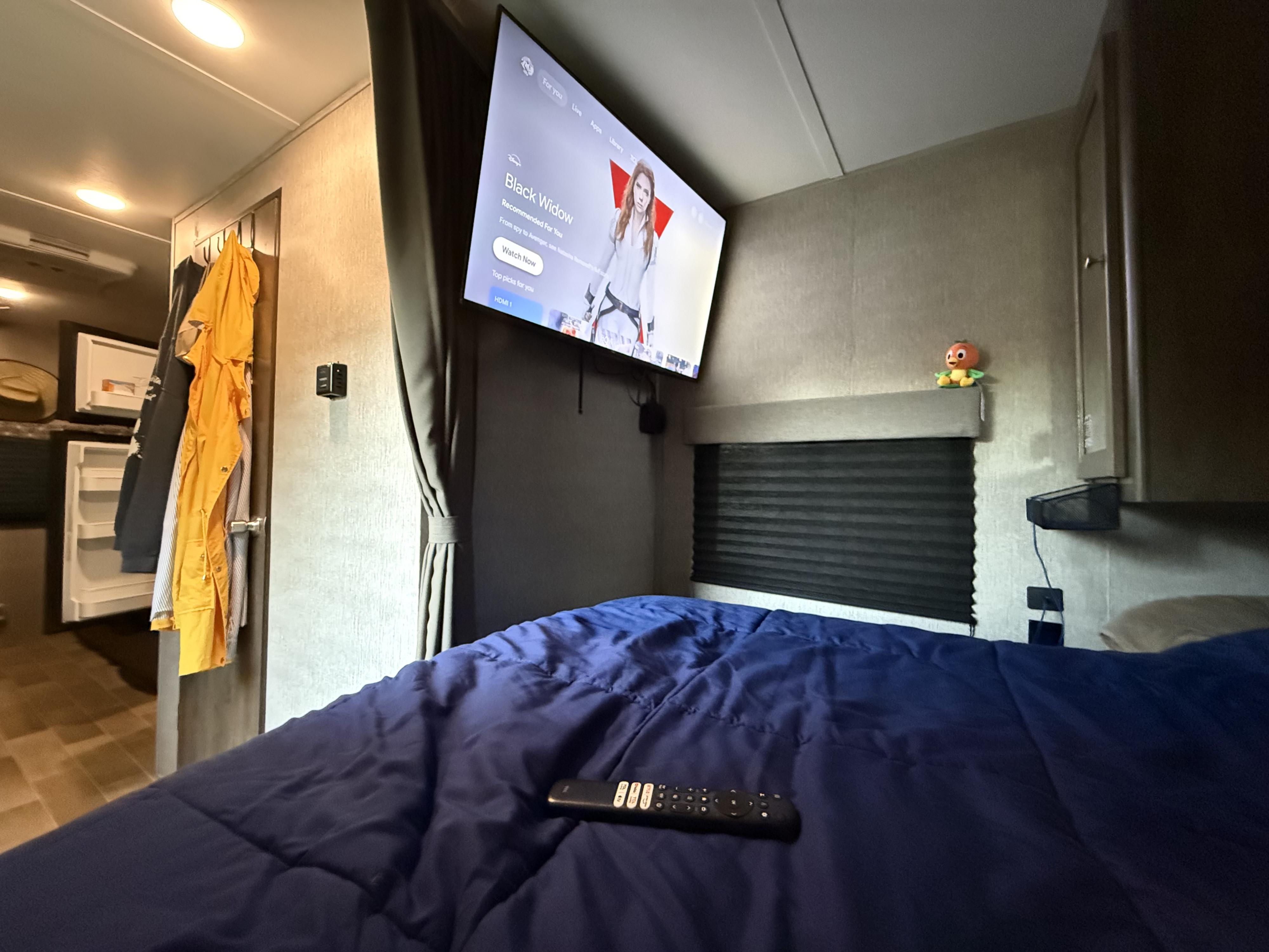 Cozy RV rental interior with a comfy bed, TV showing "Black Widow. Dutchmen Coleman Lantern LT 2020