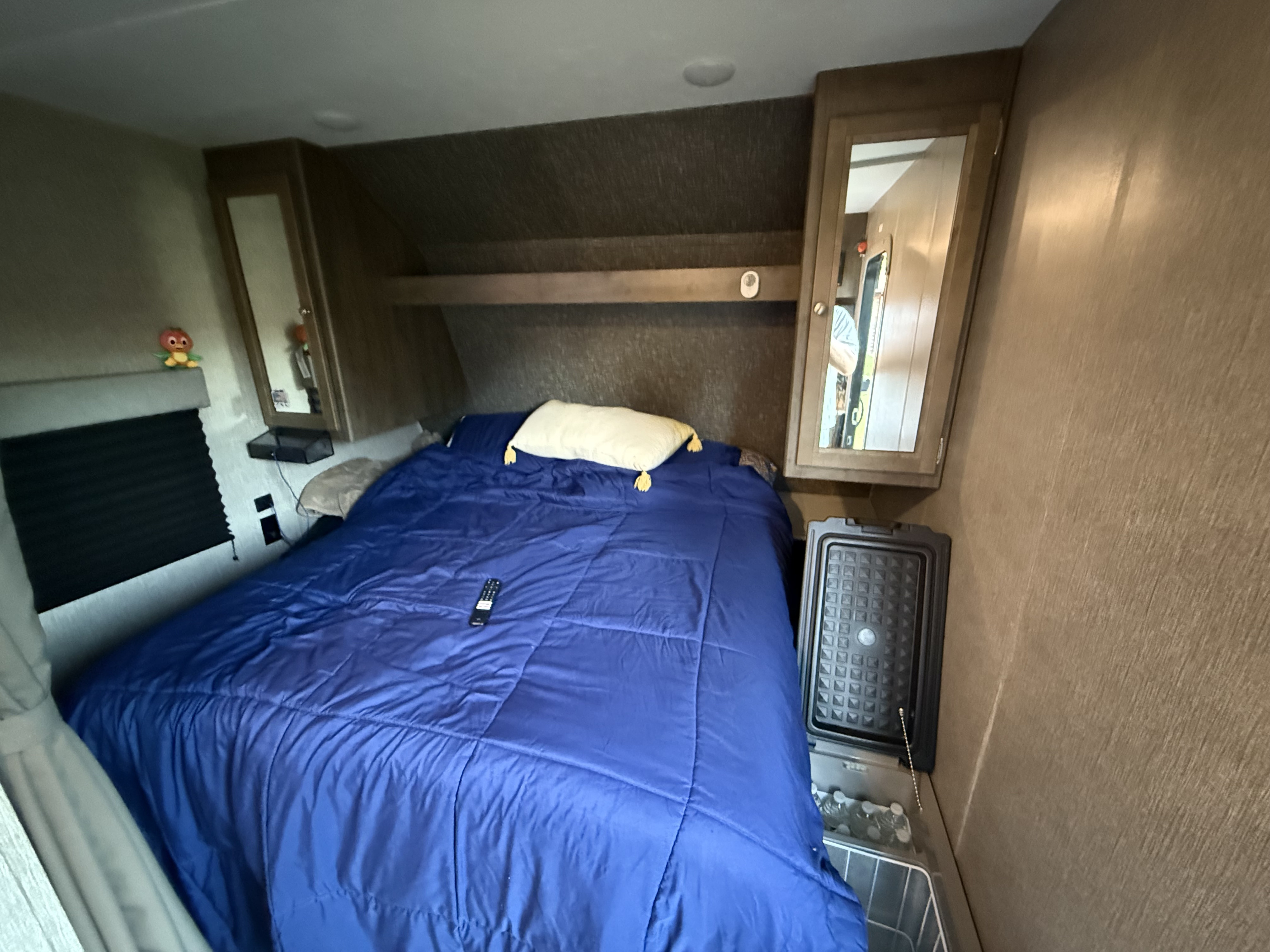 This inviting RV rental bedroom features a comfy blue bed, storage, and a handy cooler. Dutchmen Coleman Lantern LT 2020