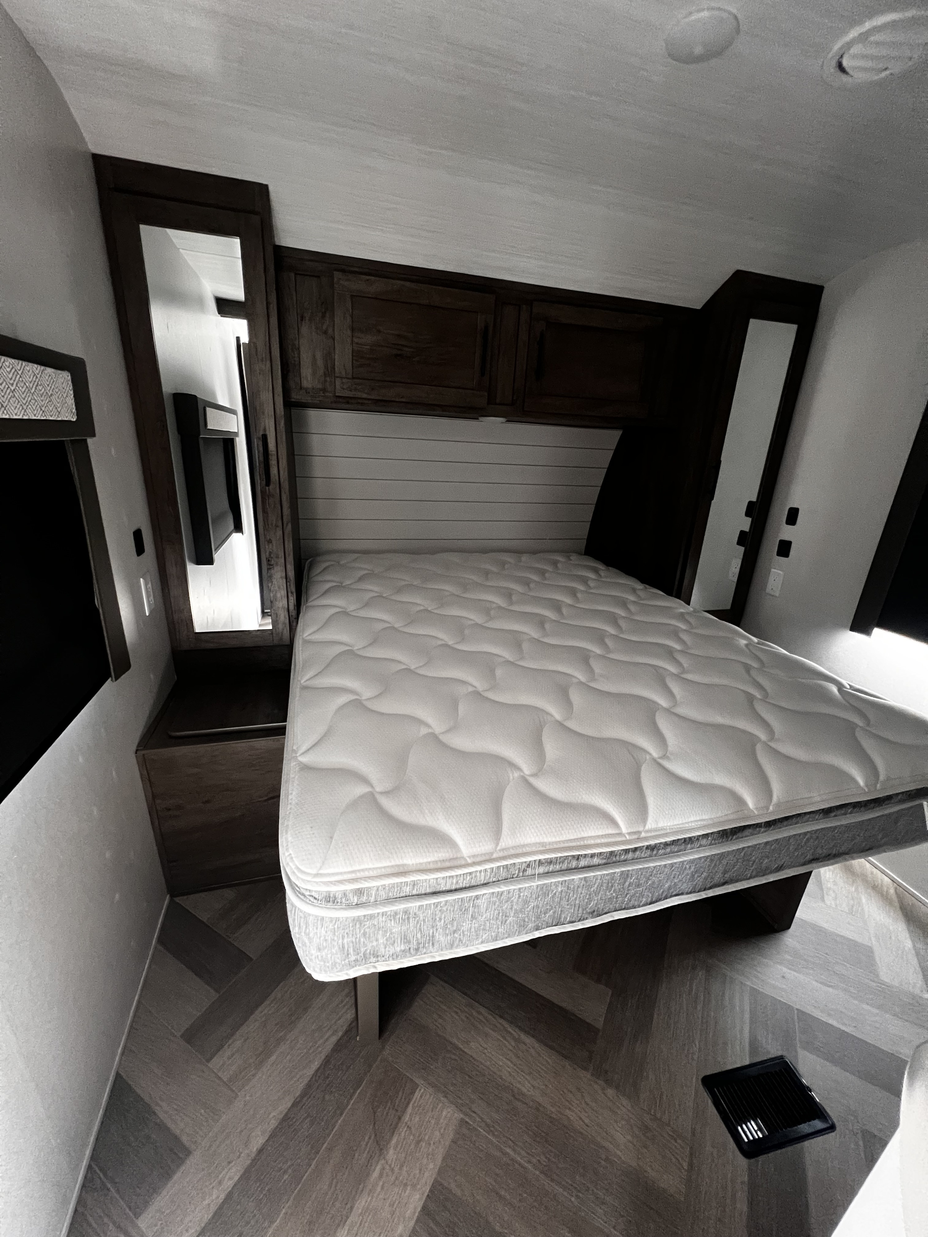 Modern RV rental bedroom featuring a comfy white mattress, dark wood accents, and herringbone flooring.. Forest River Wildwood 2022