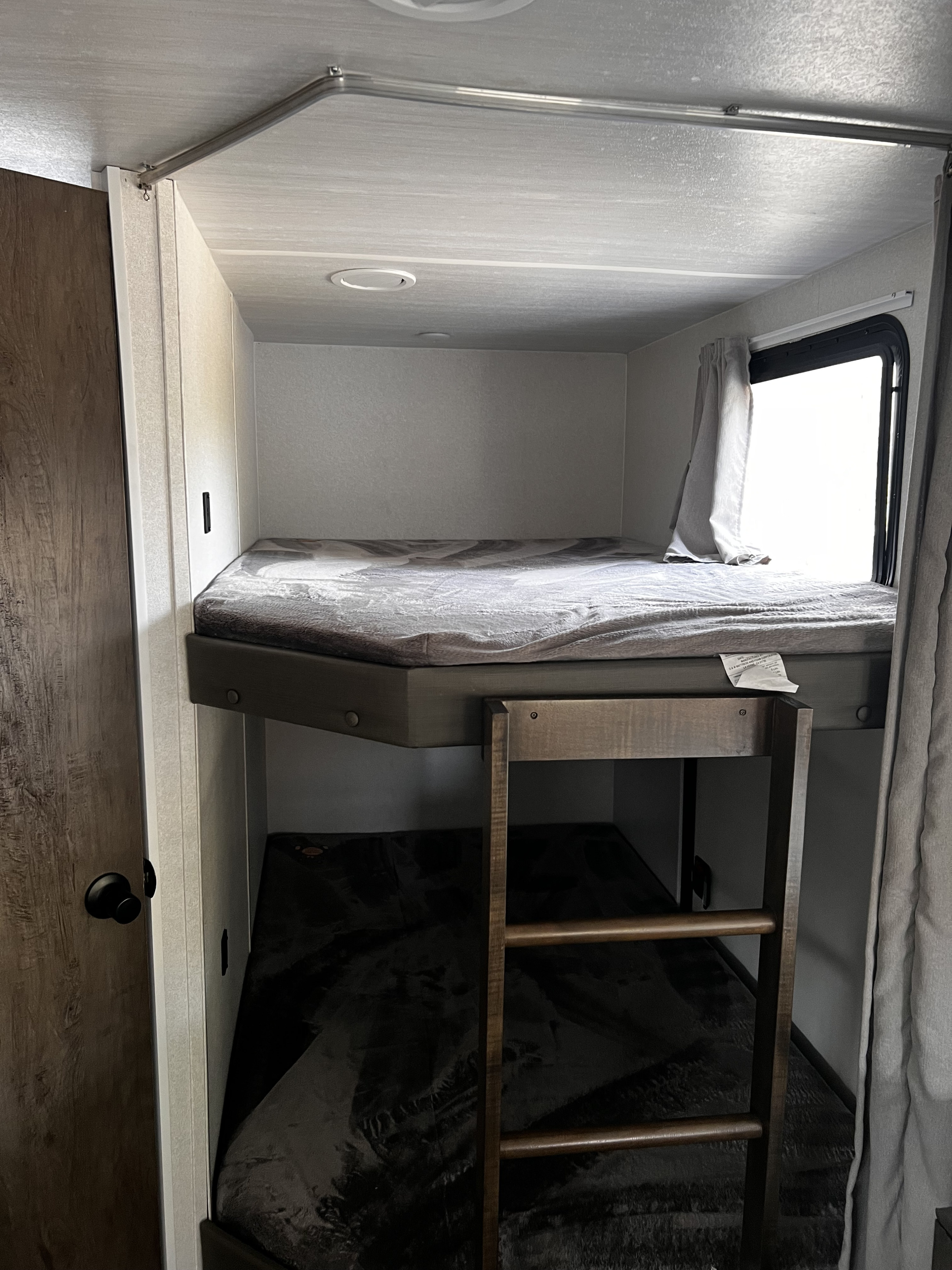 RV rental interior: bunk beds with a ladder, window, and safety bar for secure sleeping in a travel trailer.. Forest River Wildwood 2022