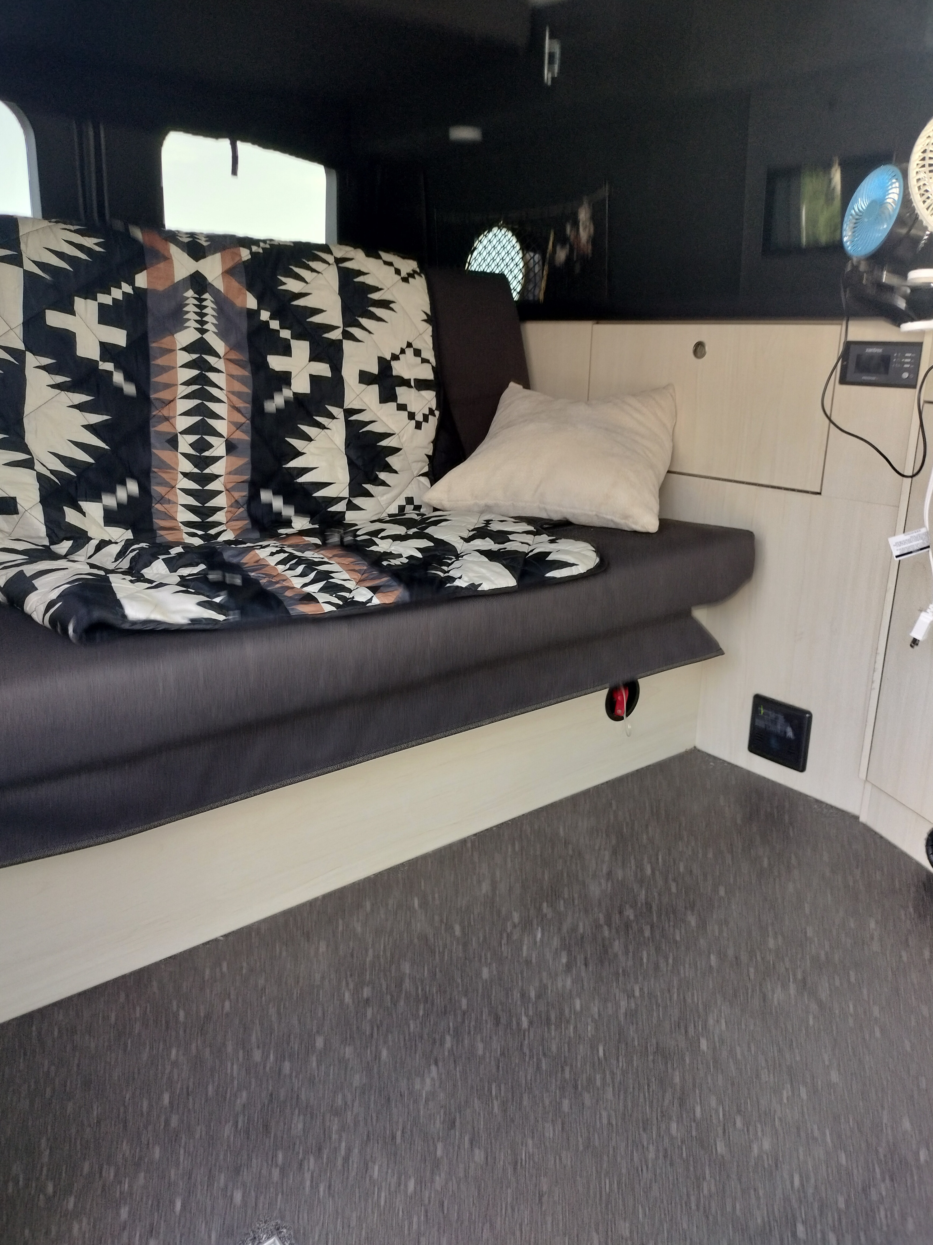 Cozy RV rental interior with patterned blanket, pillow, and portable fans. Ideal for travel.. Pleasure-Way Pleasure-Way Class B 2023