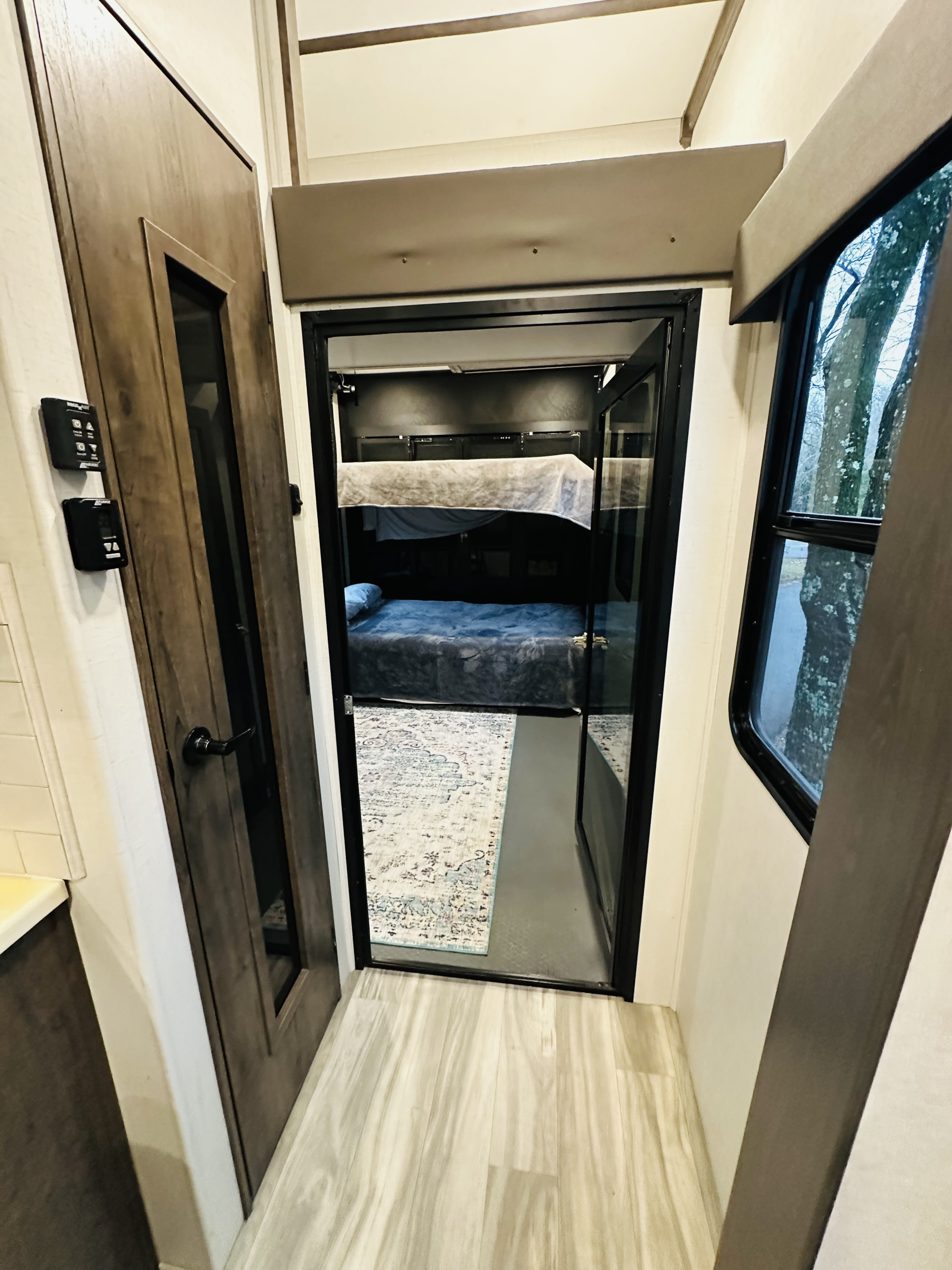Inside this RV rental: A bright hallway with light wood floors opens to a cozy bunk bed room featuring two beds.. Alliance Valor 40v13 2022