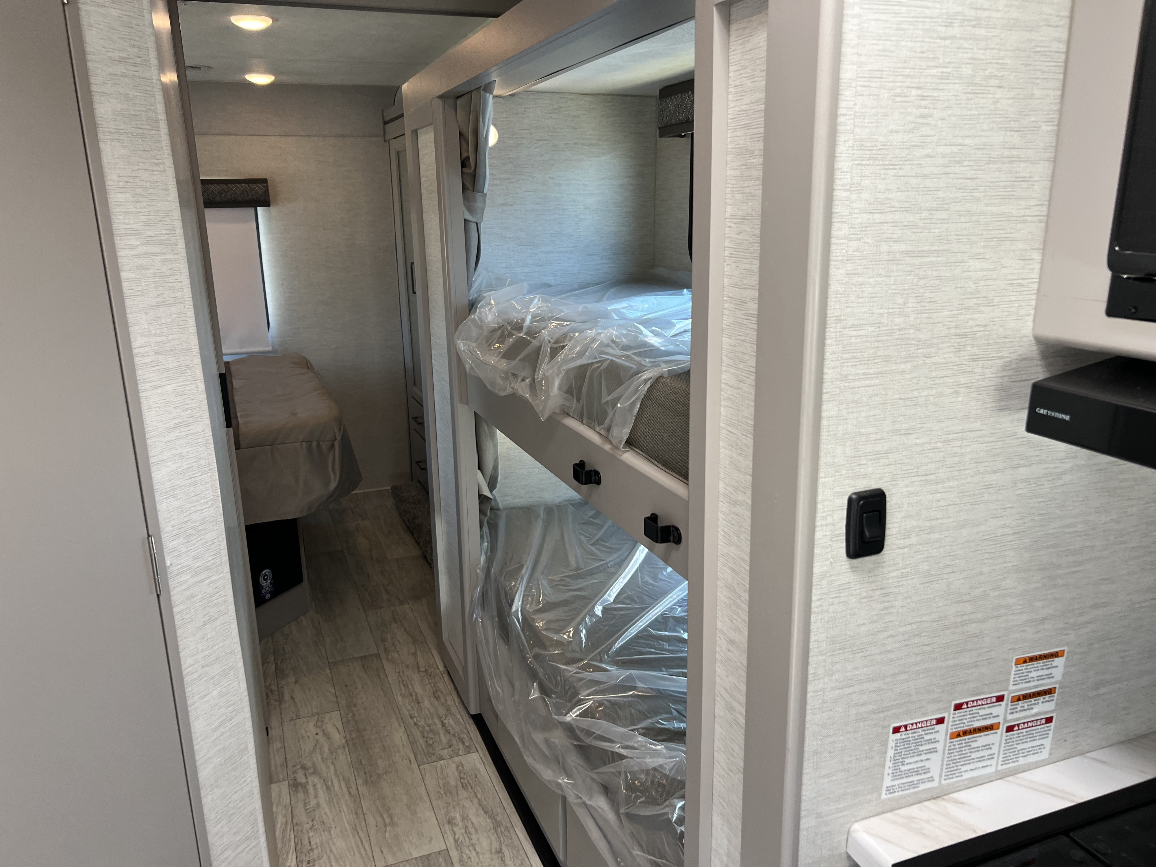 RV rental interior featuring bunk beds wrapped in plastic, a hallway leading to a bedroom, and a kitchen area with appliances.. Thor Motor Coach Chateau 2024