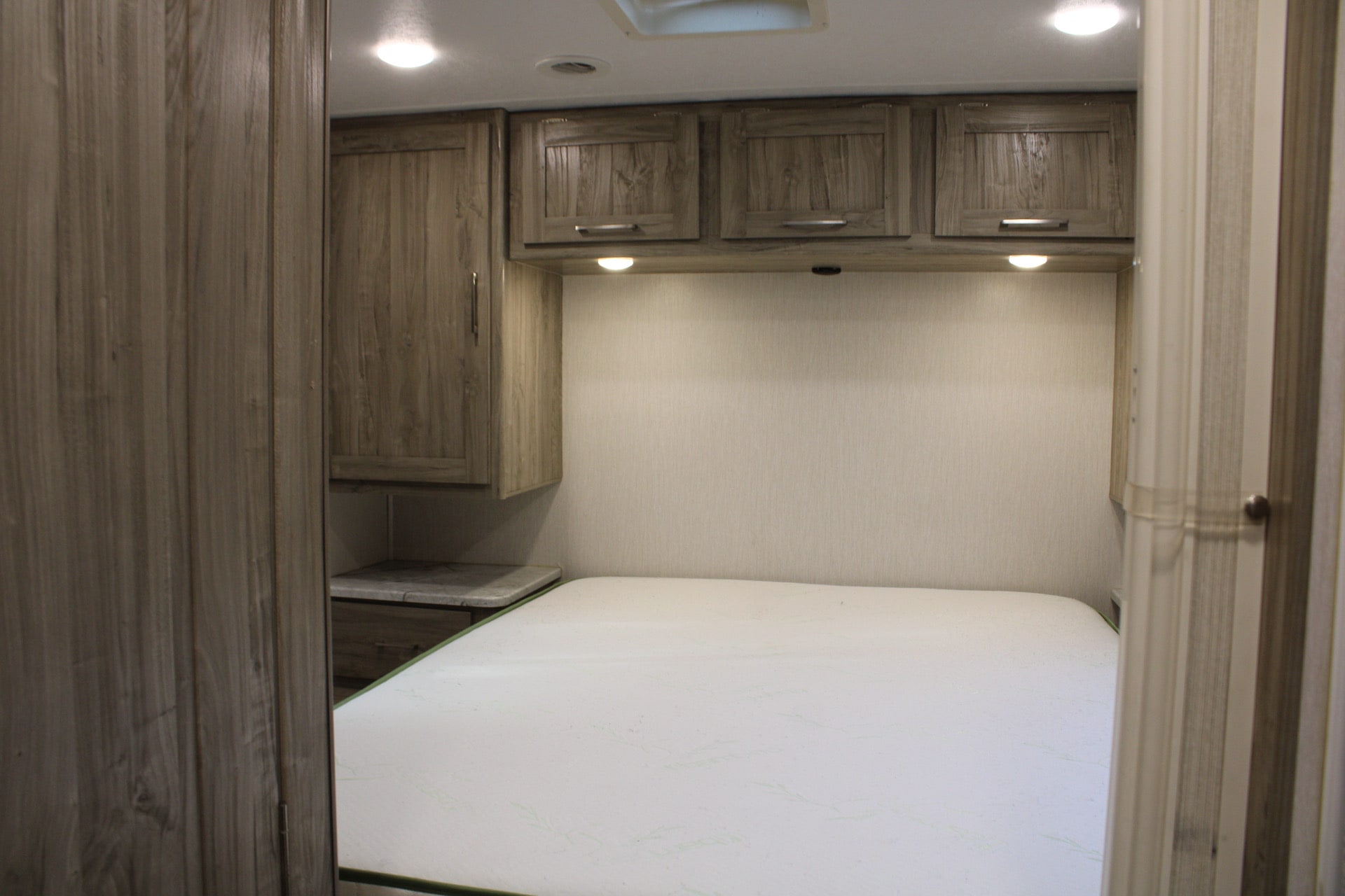 Inside an RV rental: a cozy bedroom with a mattress, wood-look cabinets, and soft lighting for your comfort.. Coachmen RV Coachmen Pursuit 27XPS 2020